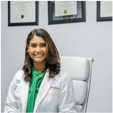 A woman wearing a white lab coat and a green scarf is sitting in a chair.