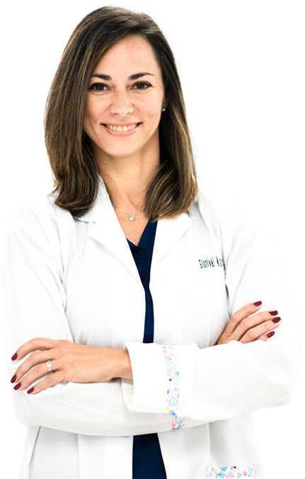 A woman in a lab coat is standing with her arms crossed and smiling.