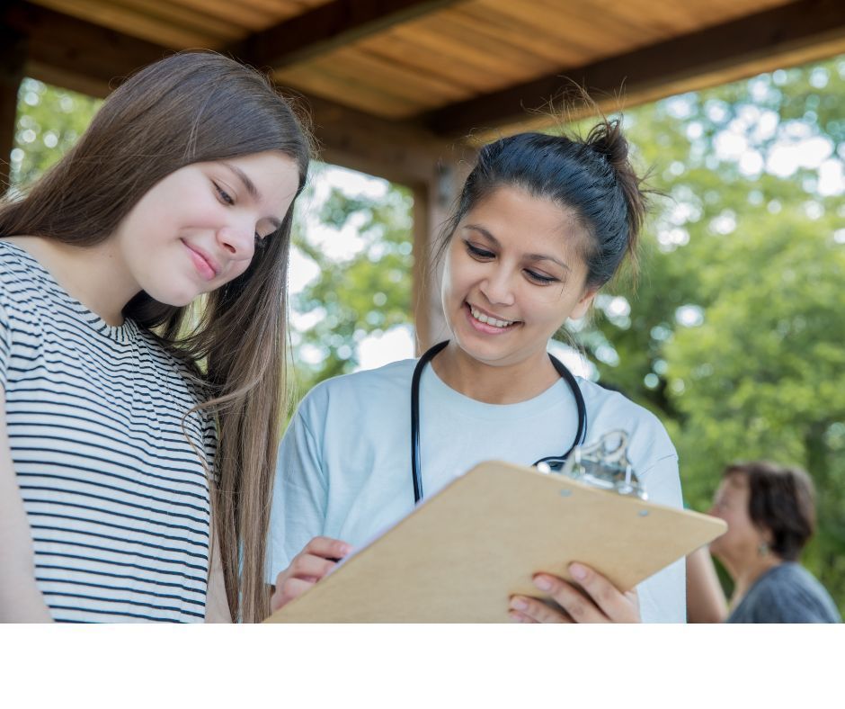 Two women are looking at a clipboard under a canopy.