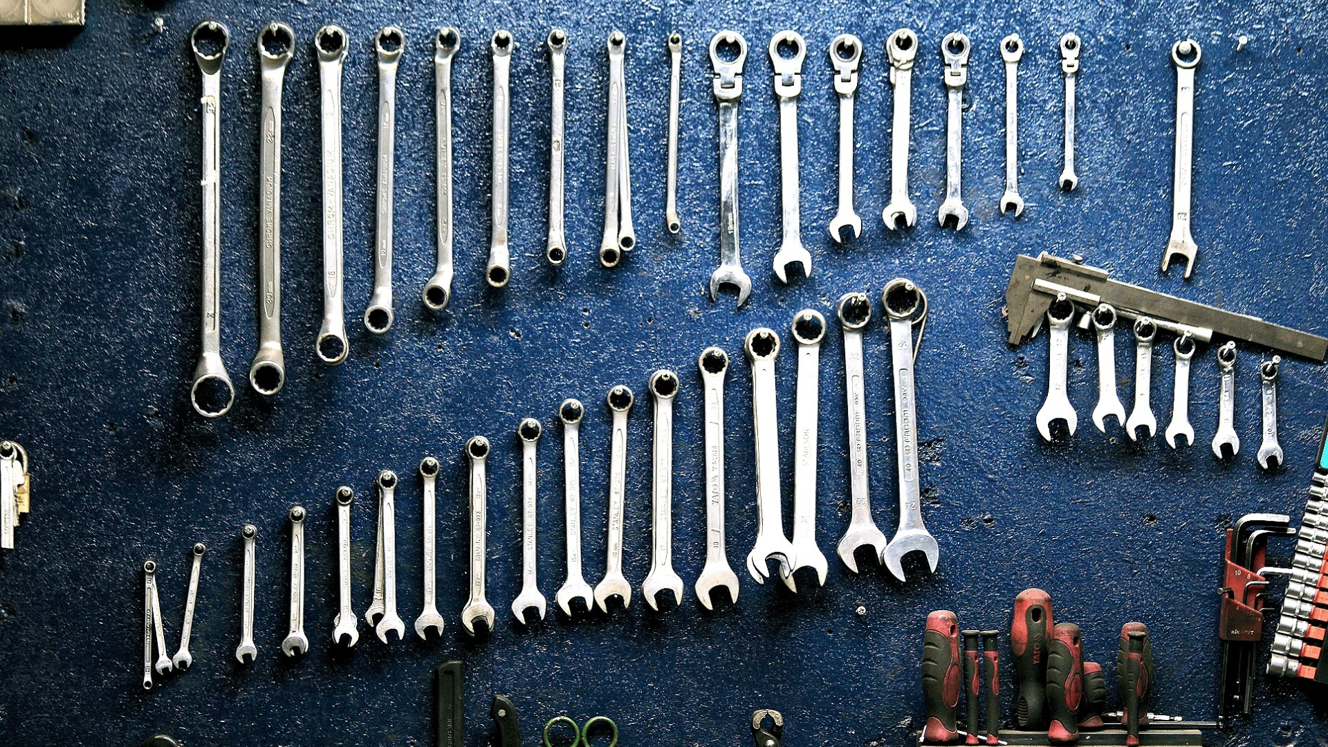 A bunch of wrenches are hanging on a blue wall