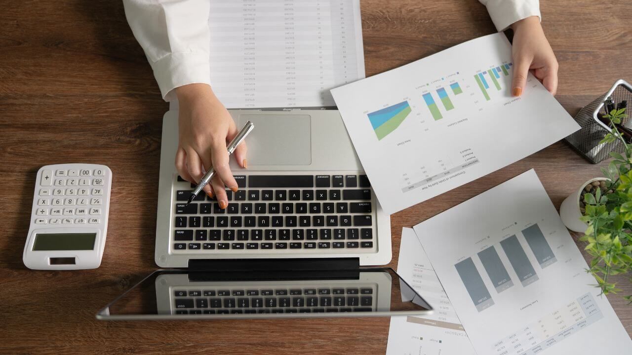 Businesswoman using laptop and calculator with paperwork on desk.