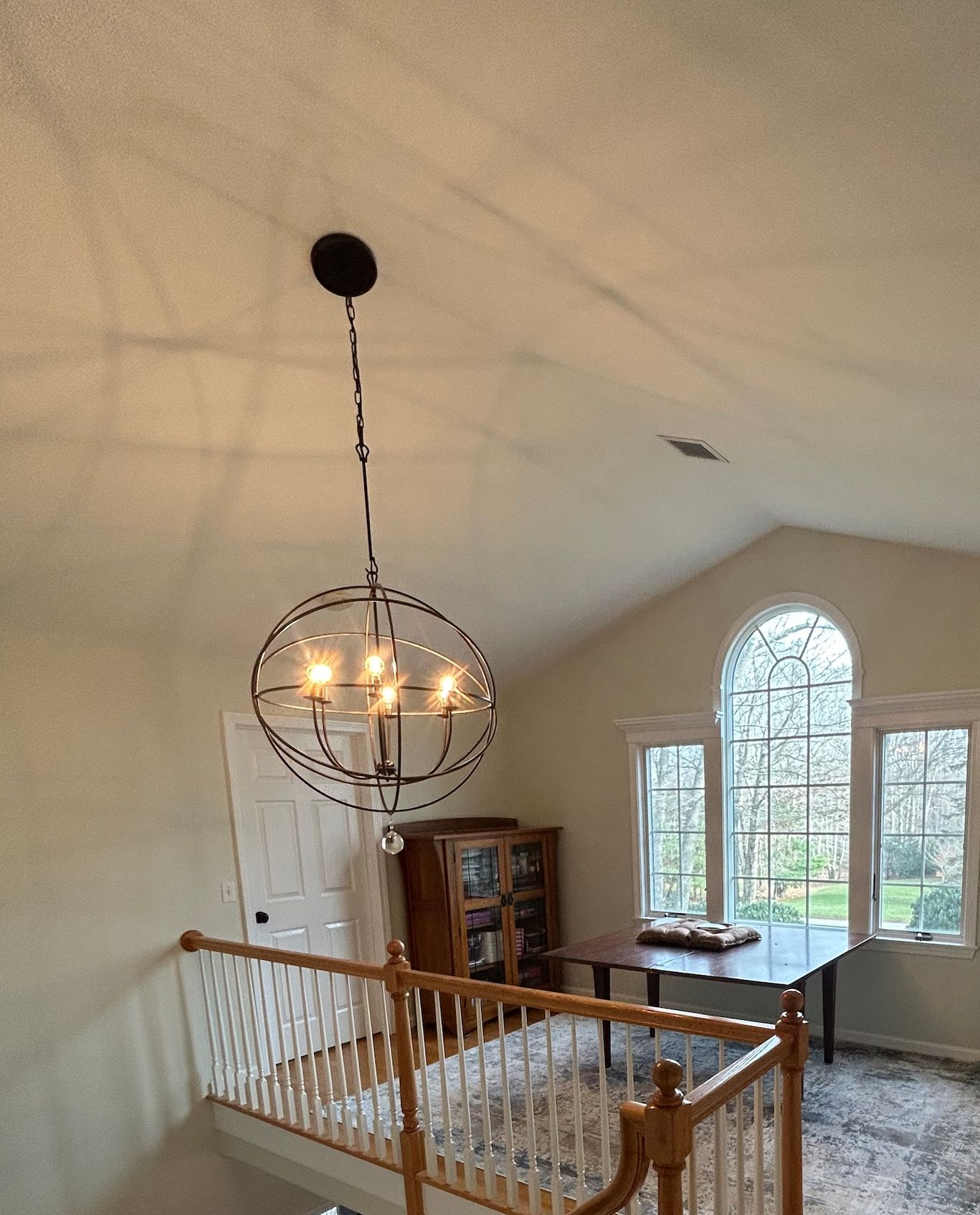 Looking down a staircase in a house with a chandelier and a reading area.