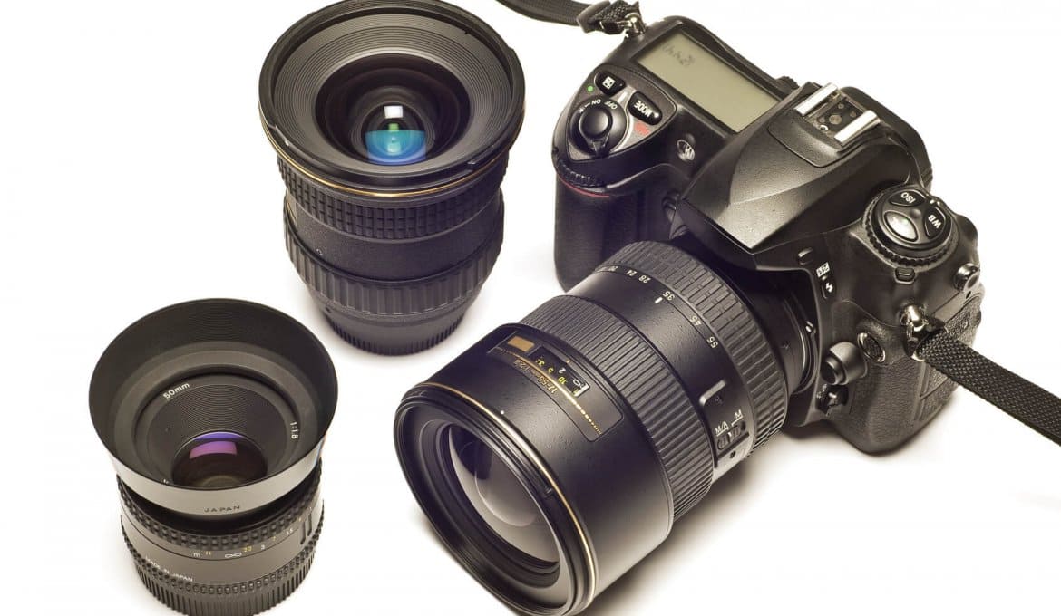 Câmera e lentes sobre fundo branco, ilustrando equipamentos fotográficos.