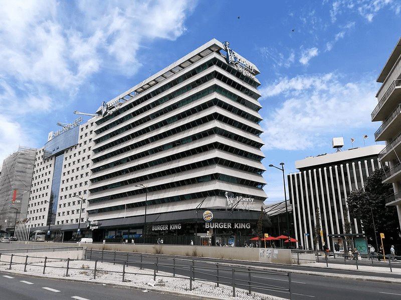 Prédio moderno com um Burger King no térreo, sob um céu parcialmente nublado.