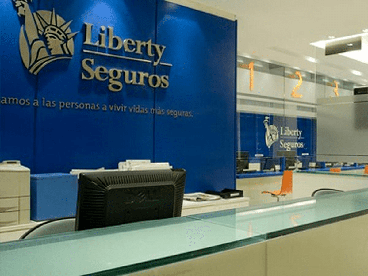 Interior do escritório da Liberty Seguros com paredes azuis, logotipo e balcão de recepção.