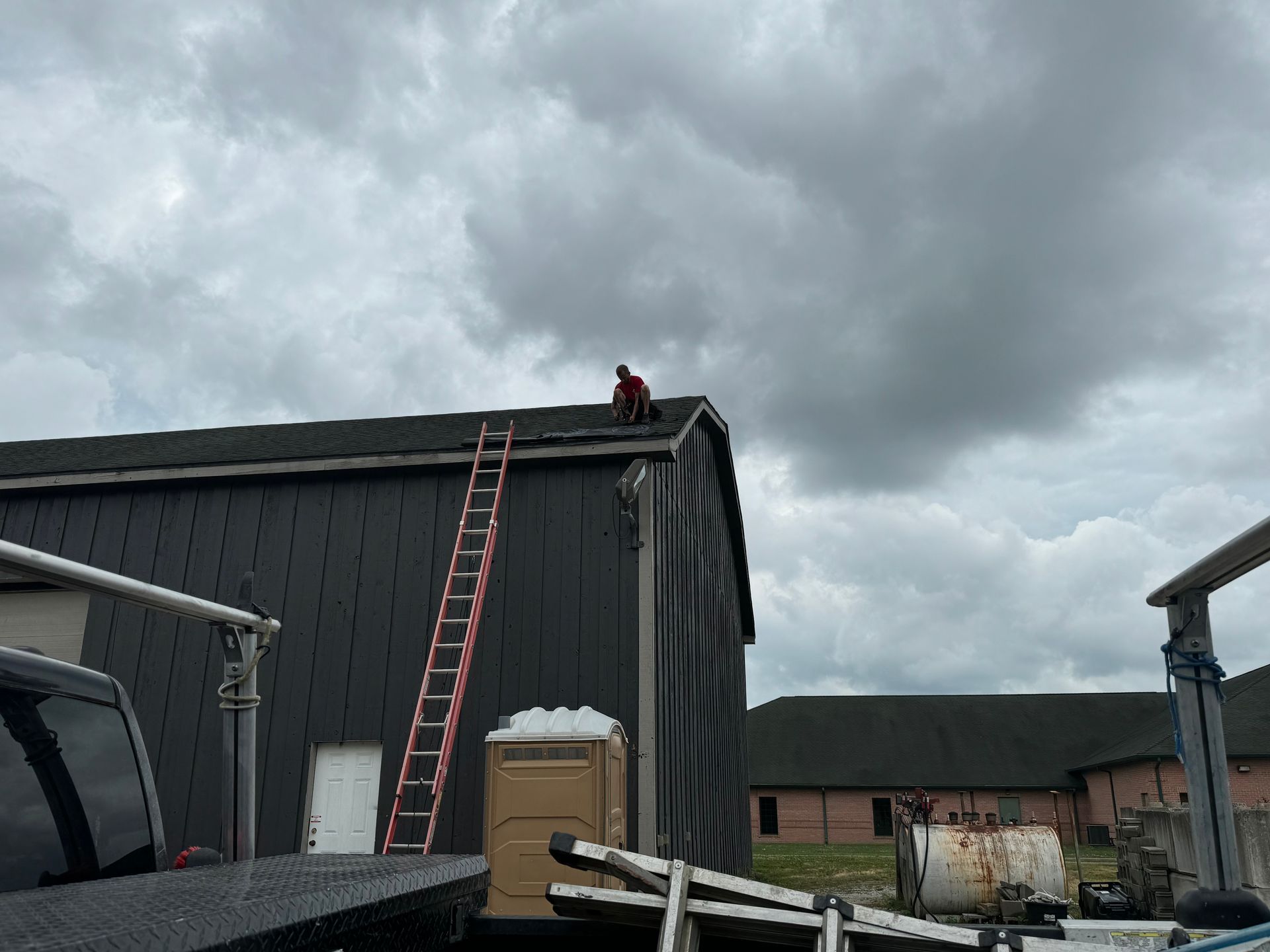 A man is standing on the roof of a building with a ladder.
