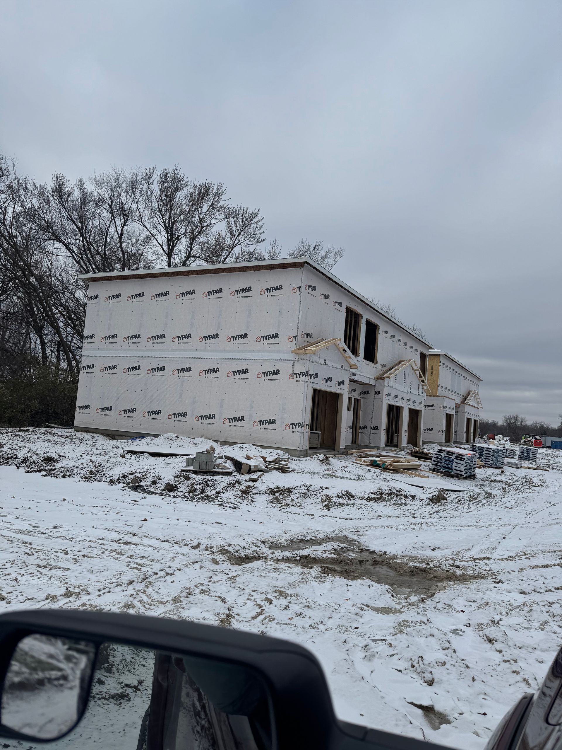 A car is driving down a snowy road in front of a building under construction.