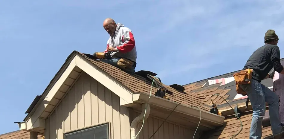 Two men are working on the roof of a house.