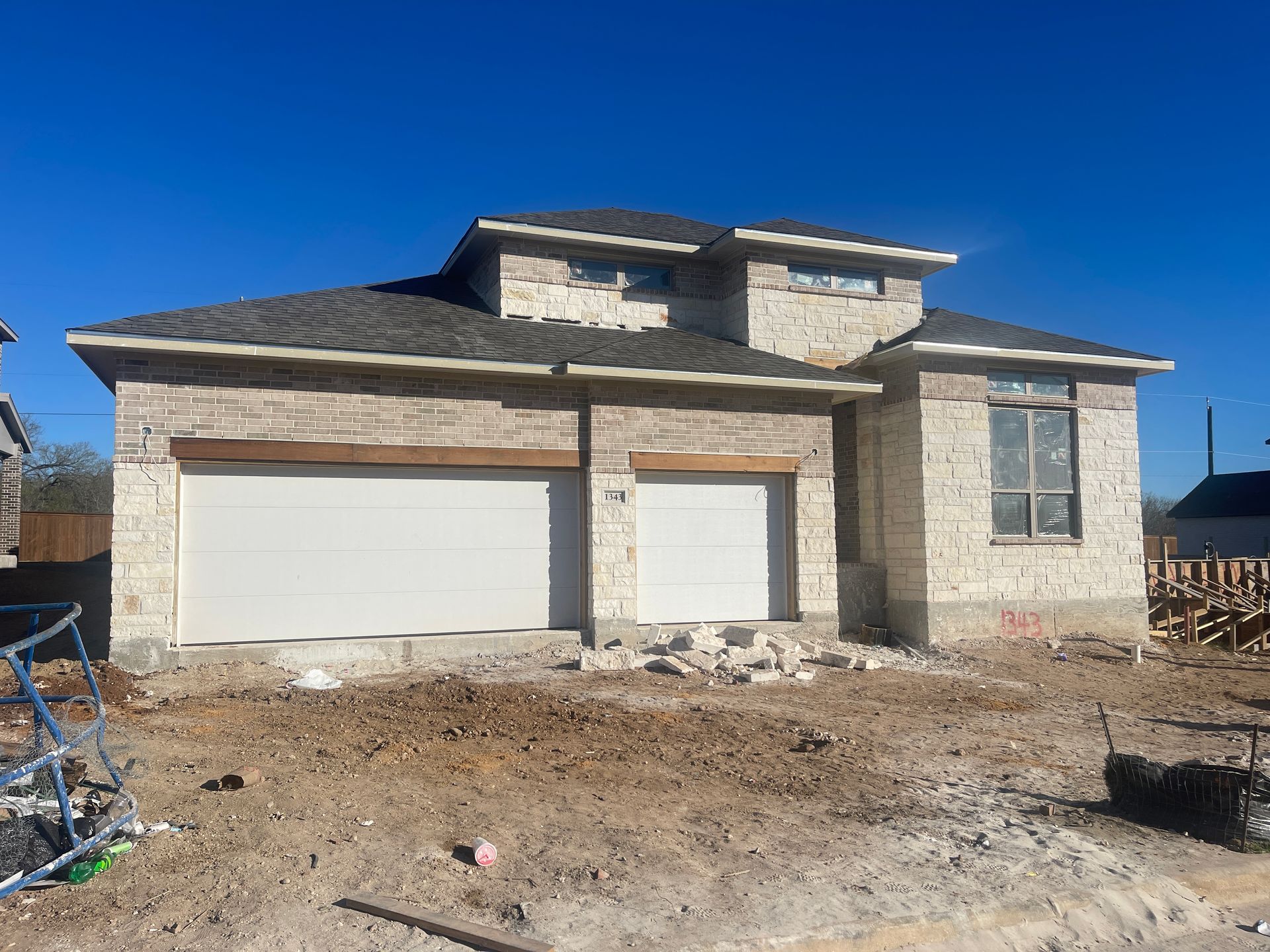 New house under construction; beige stone exterior, white garage doors, and clear blue sky.