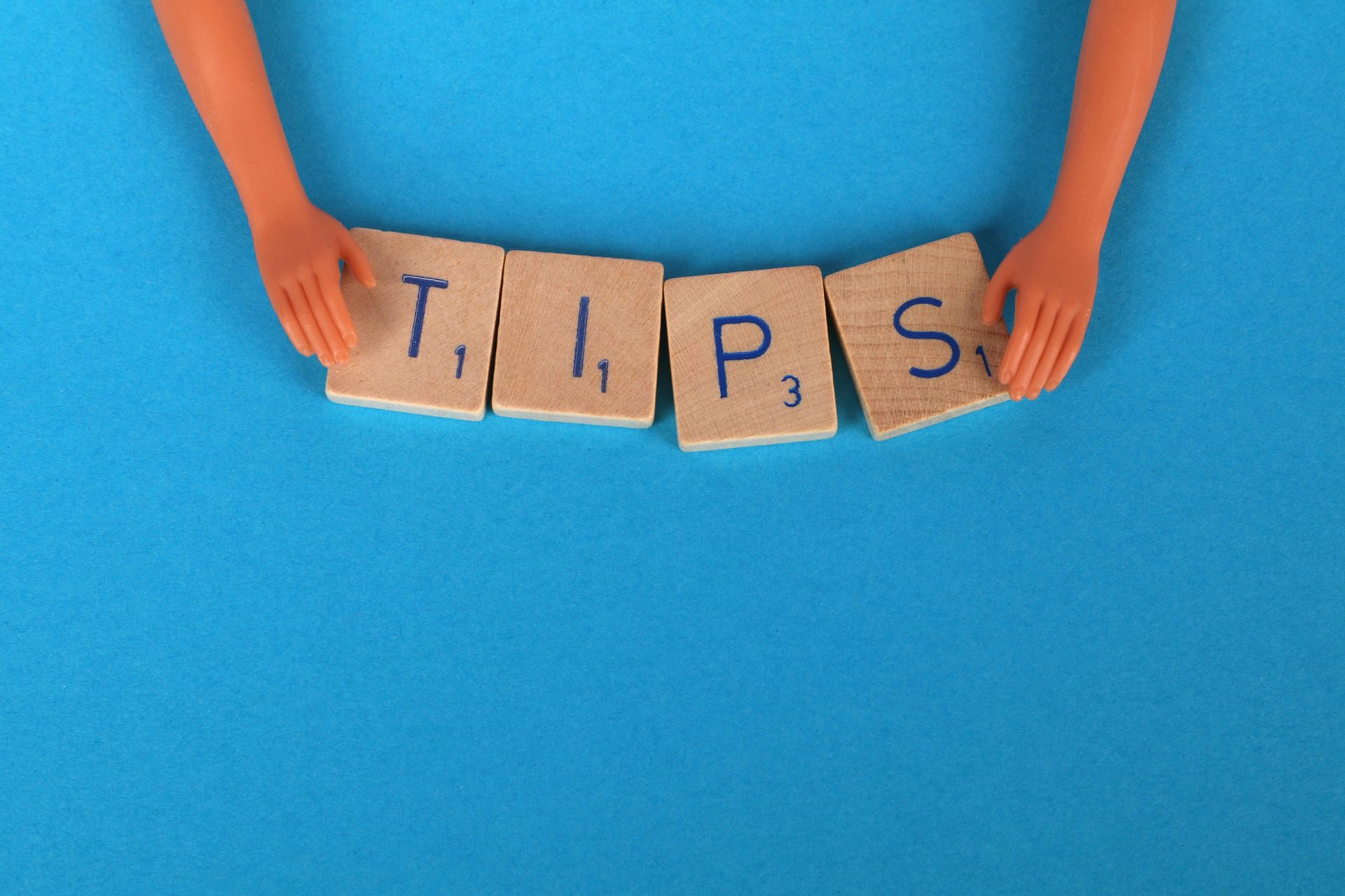 Hands holding wooden tiles spelling “Tips” on a blue background