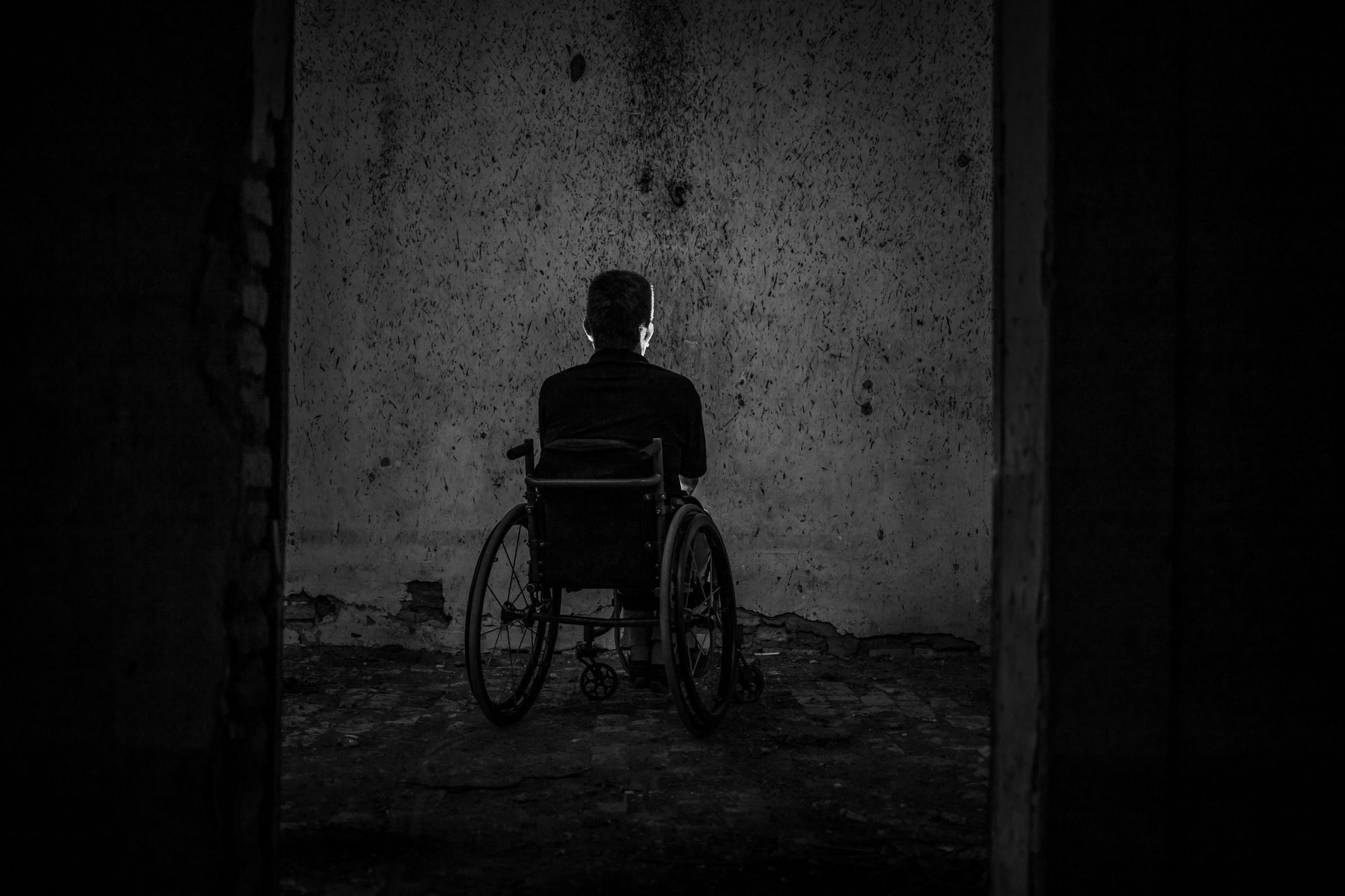 Person in wheelchair facing a dark wall. Black and white image.