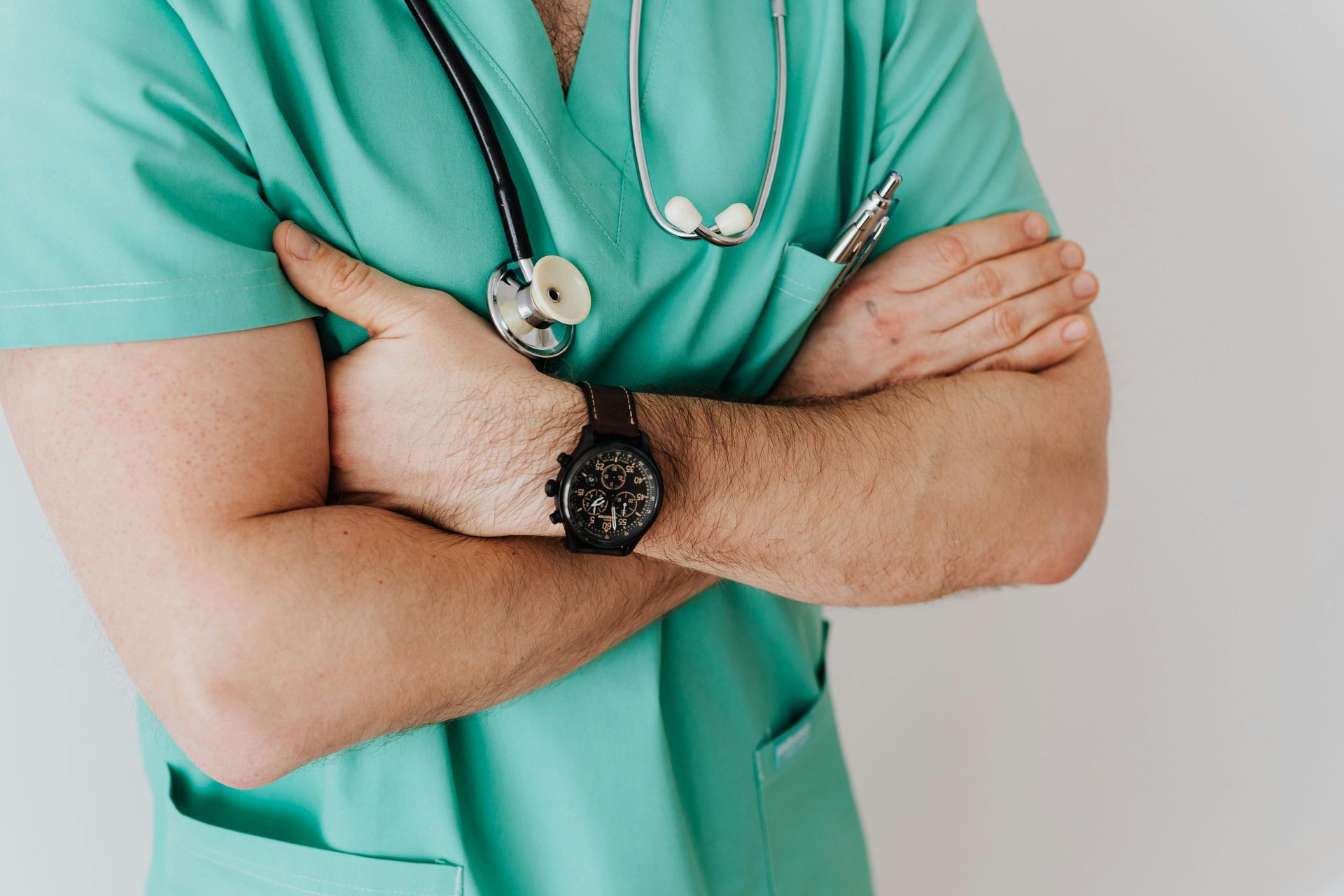Person in green scrubs with arms crossed, stethoscope, watch.
