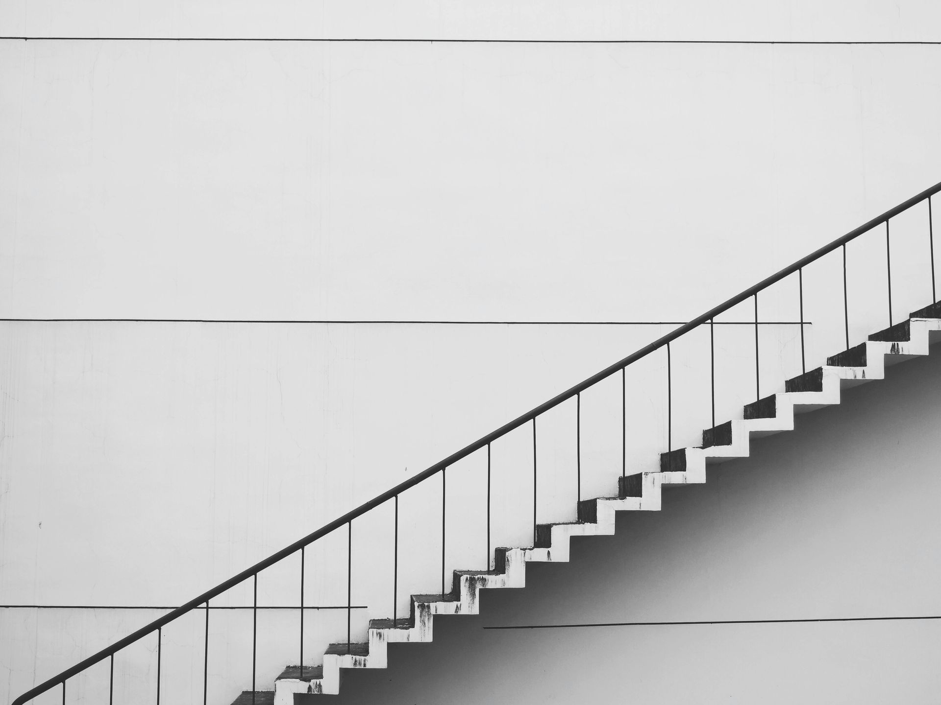 Black and white photo of a staircase against a white wall, ascending diagonally.