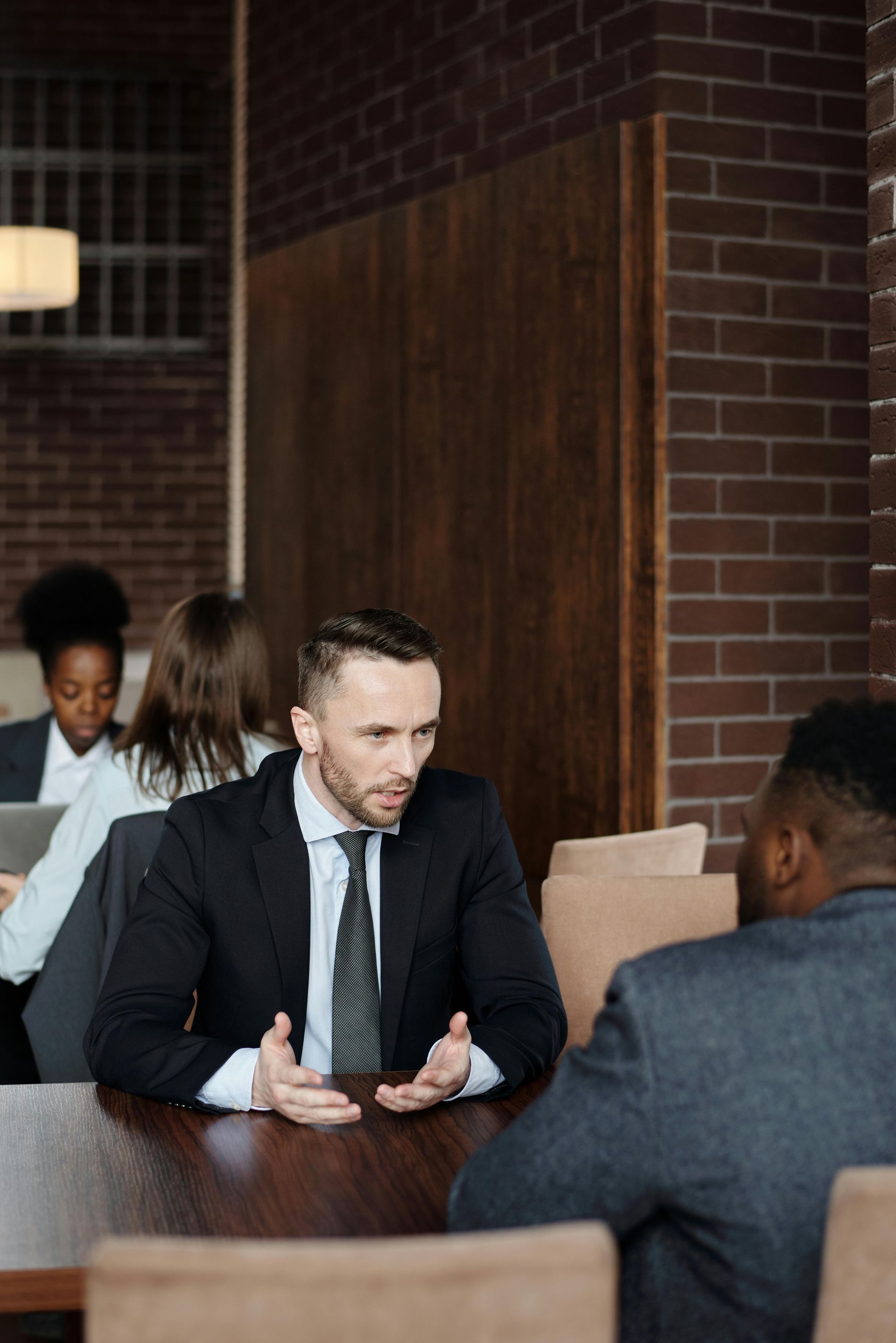 Two lawyers in suits having a conversation at a table in an office setting.