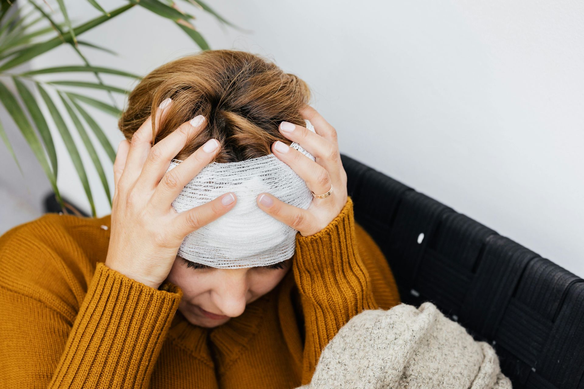 Woman wearing eye covering, holding head, looking down with distressed expression, sitting indoors.