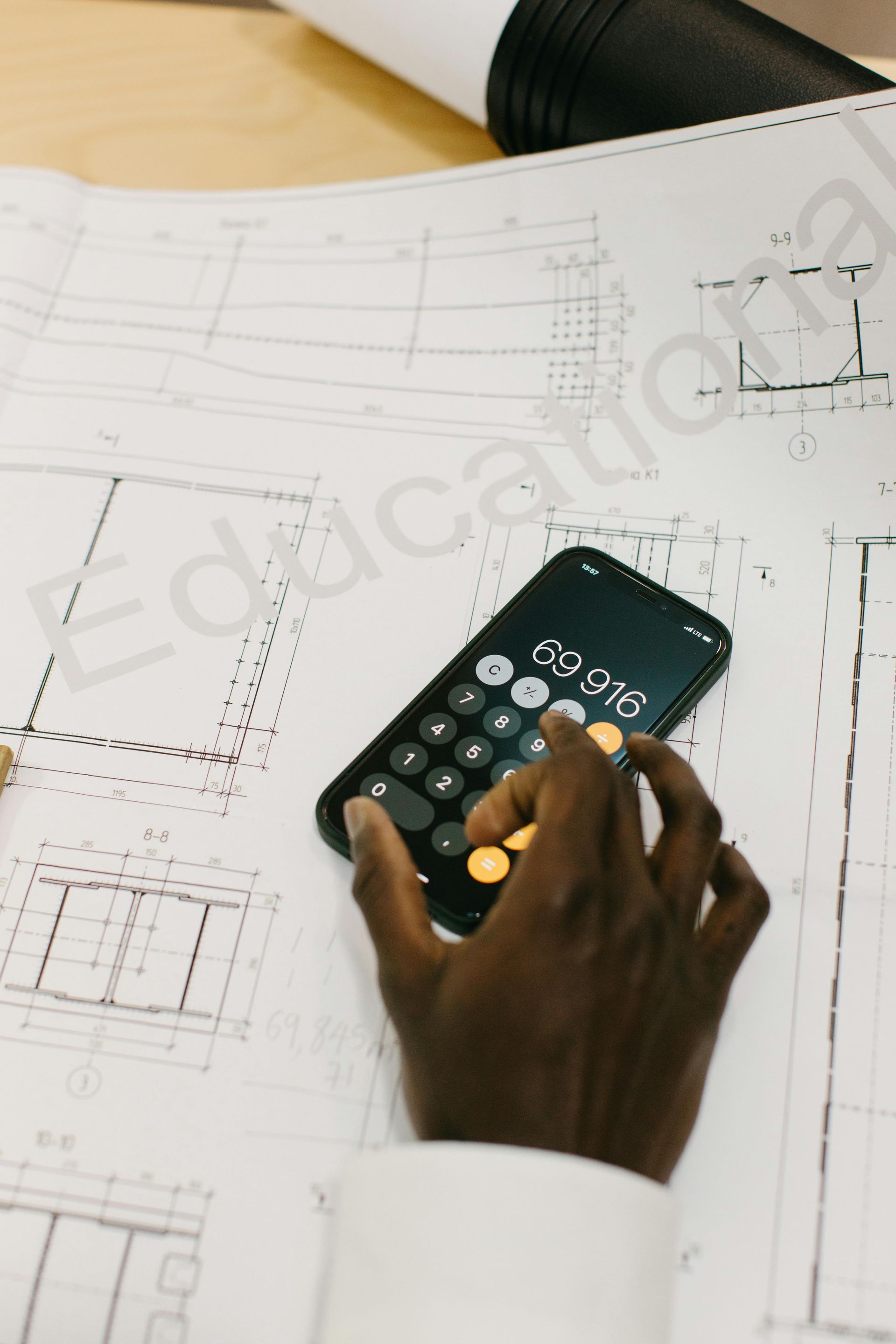 Person using a calculator on architectural blueprints, calculating numbers, close up.