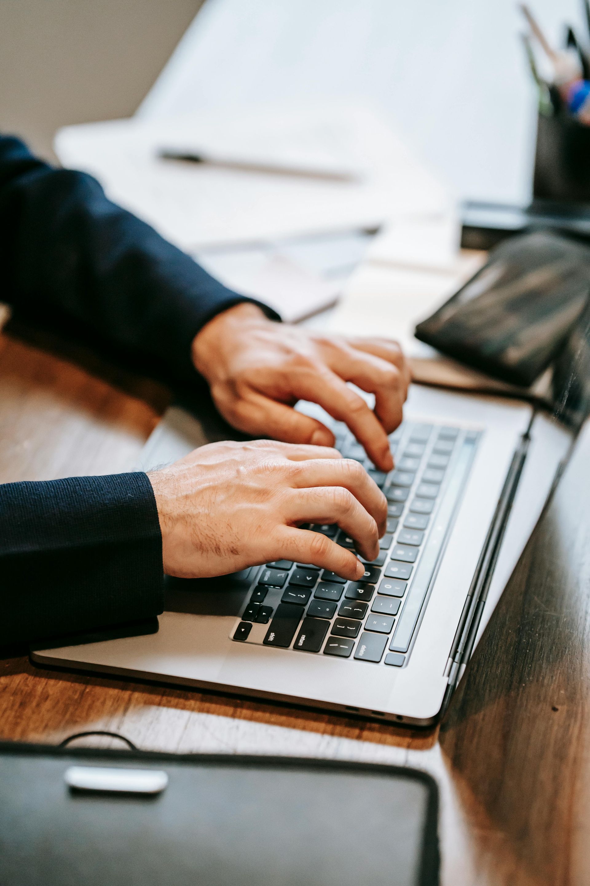Person in a suit typing on a laptop at a desk, hands visible.