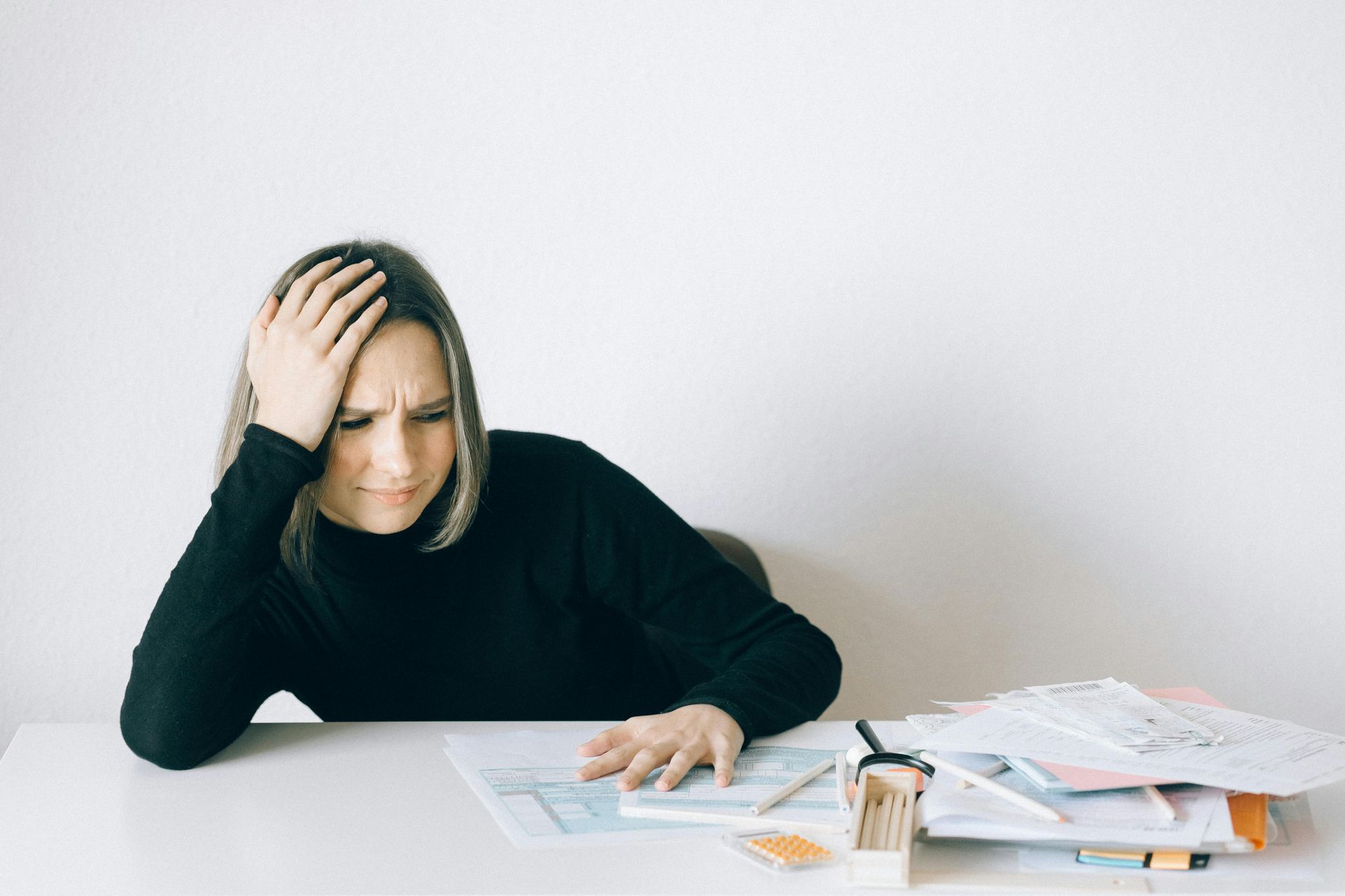 Woman with hand on forehead, looking stressed at paperwork on a desk.