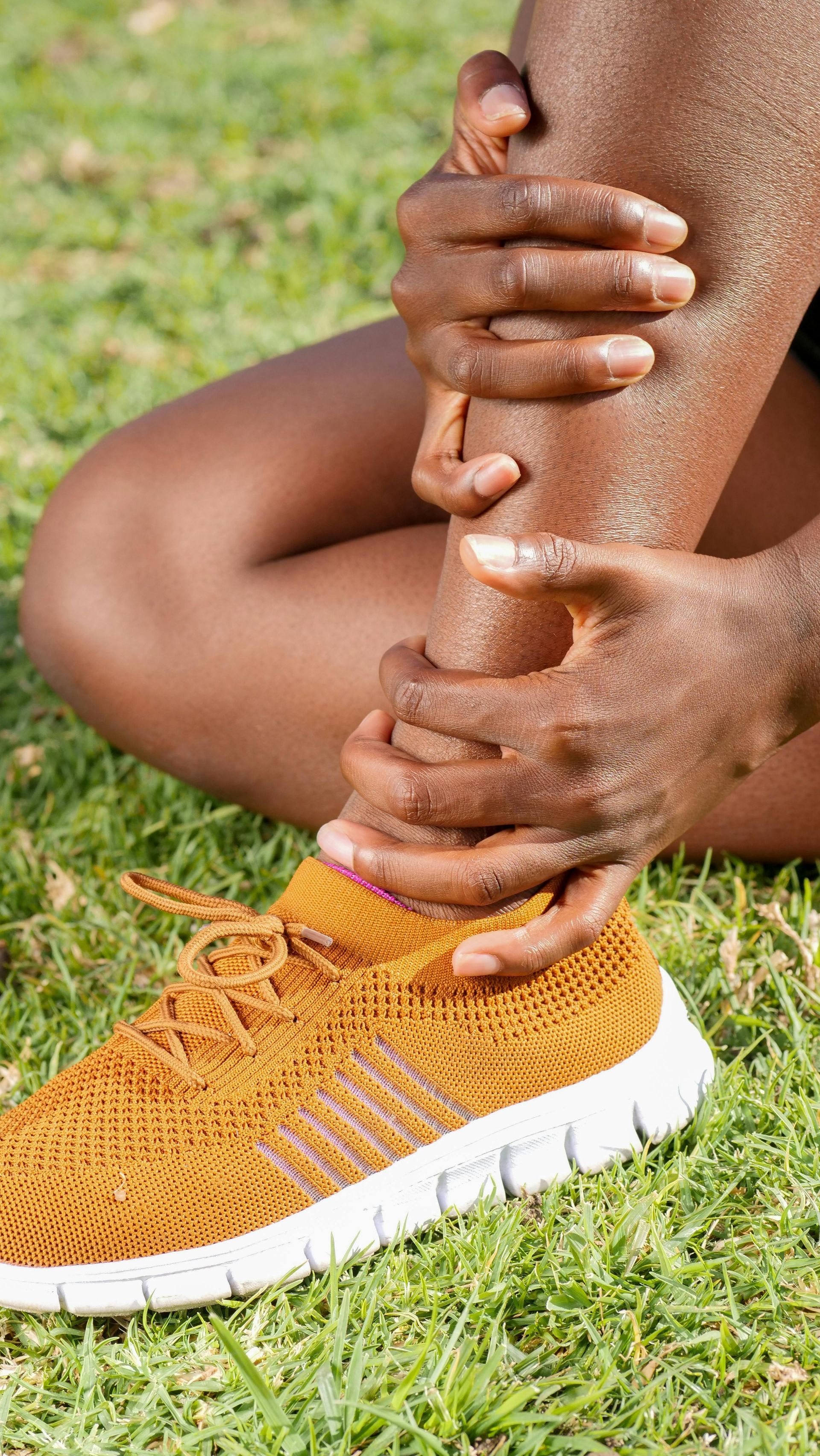 A person is holding their ankle in pain while sitting on the grass.