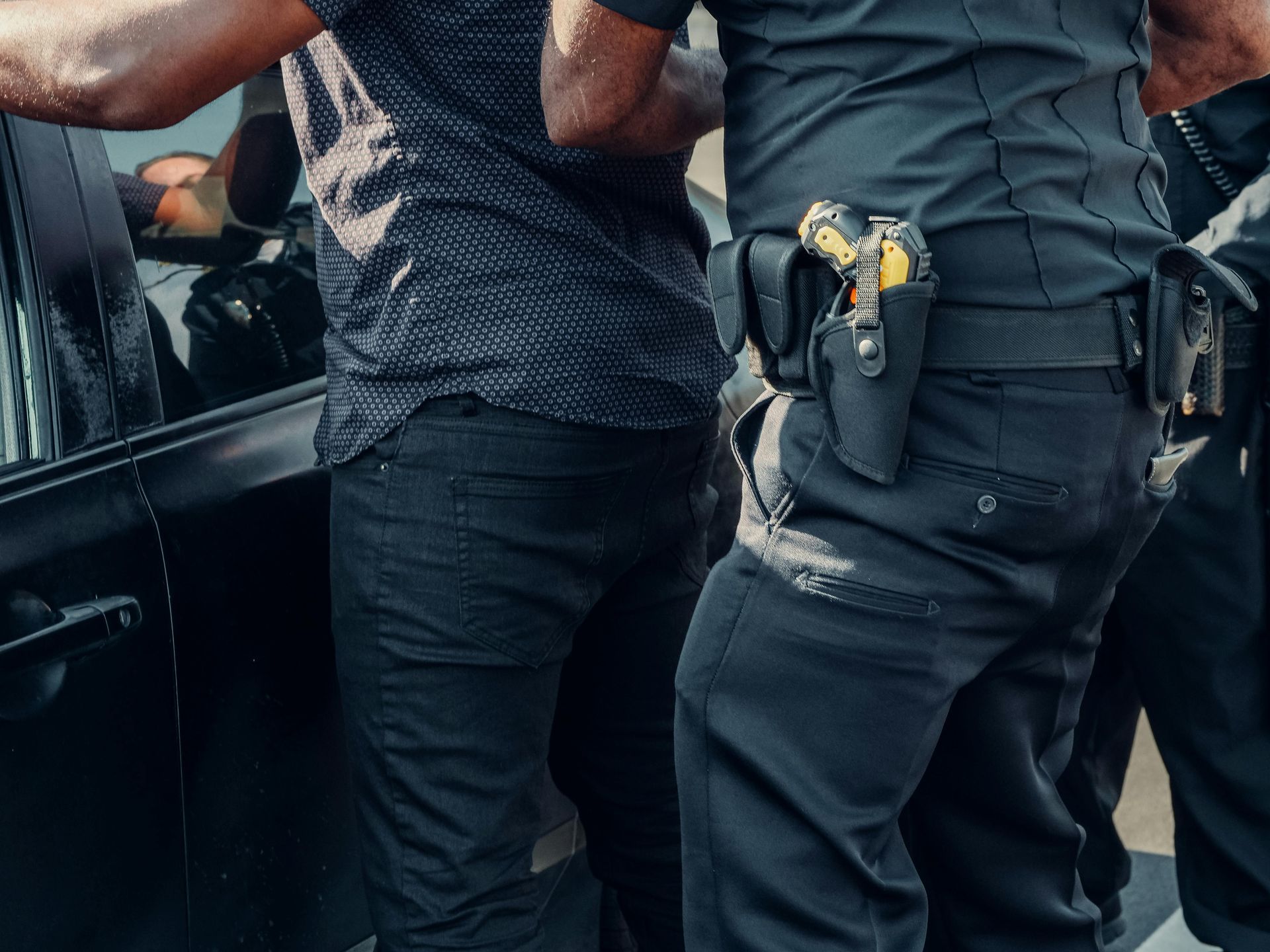 A picture of a police officer putting an alleged felon under arrest by the arrestees car.
