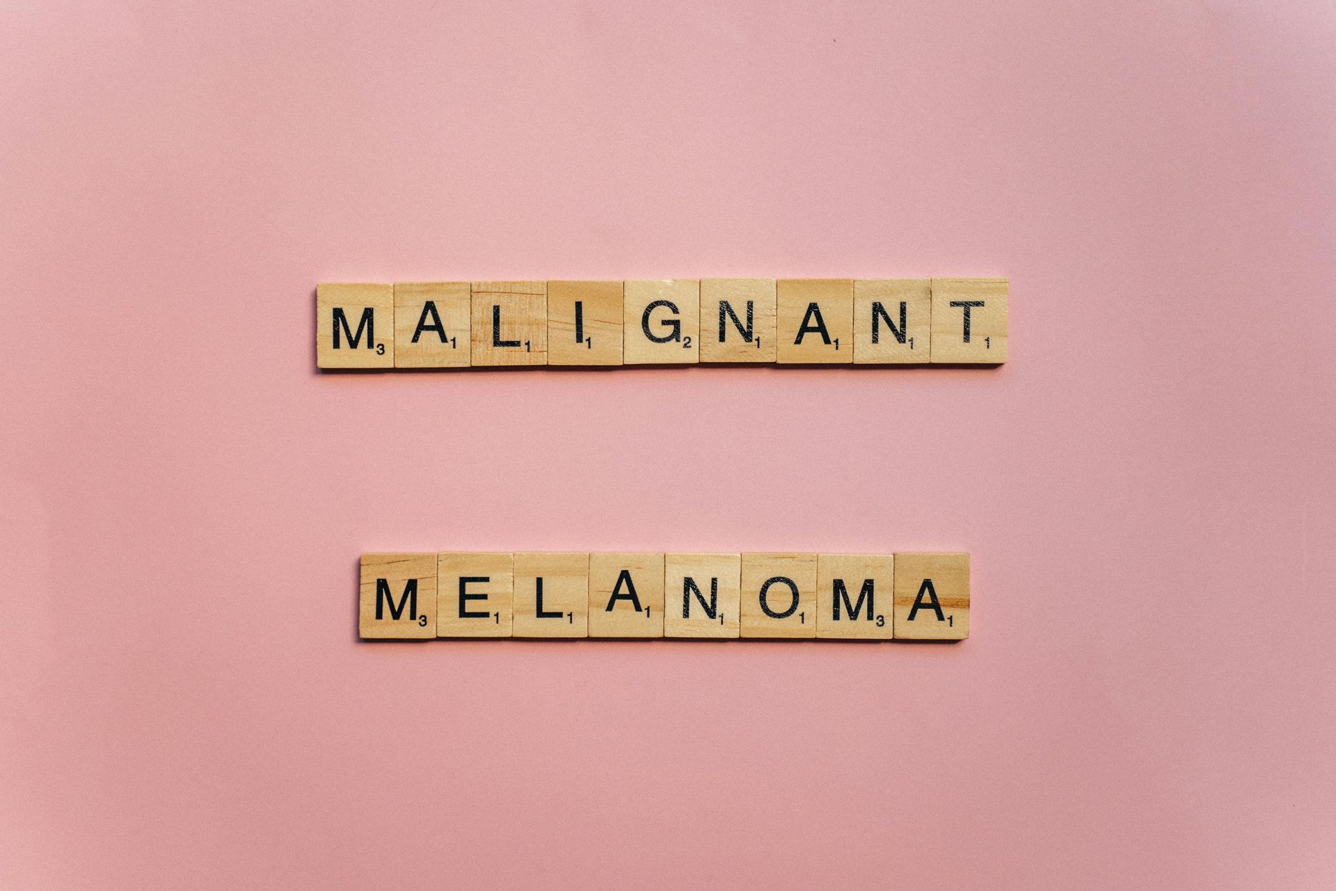 The word melanoma is written in scrabble tiles on a pink background.