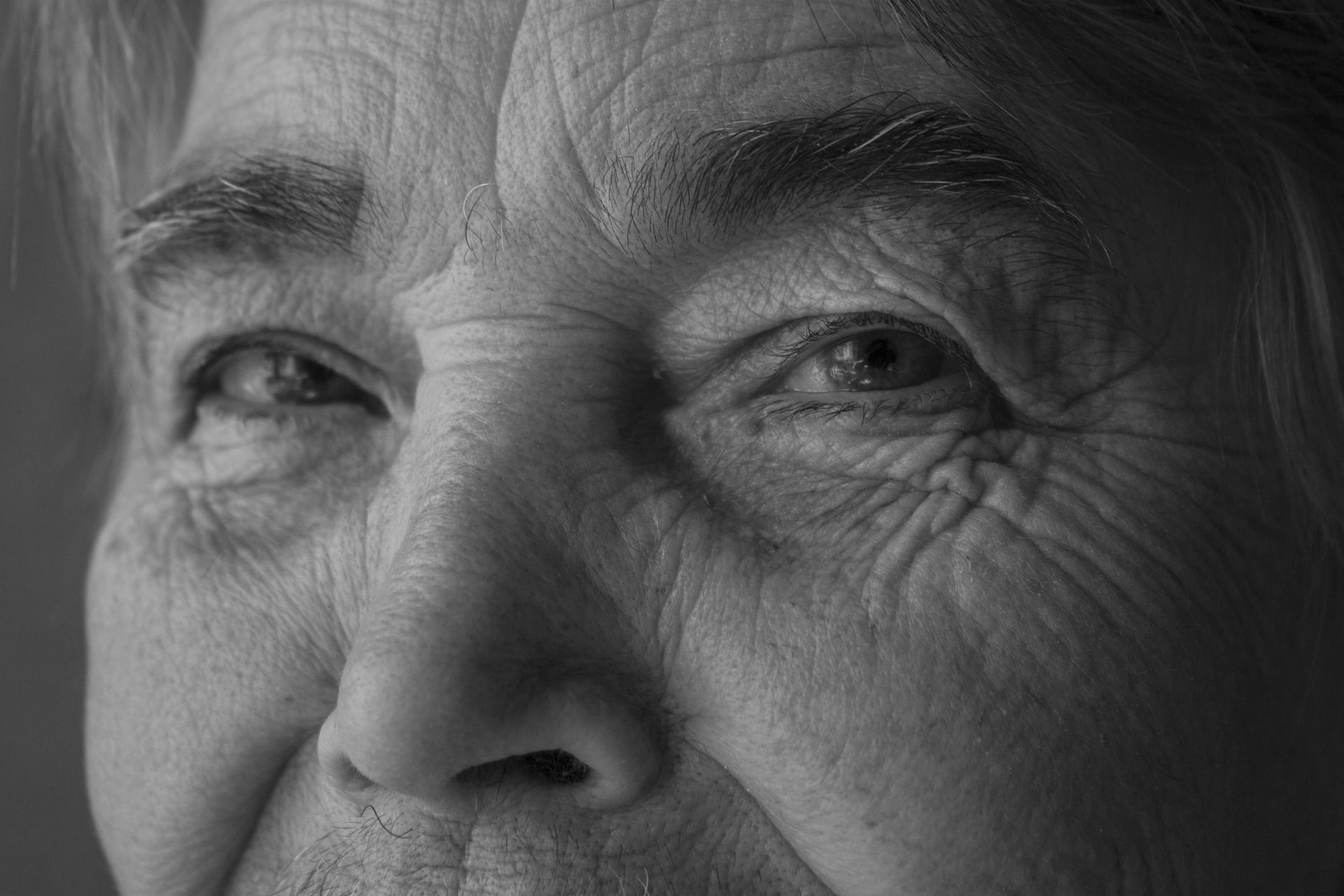 Close-up black and white of an elderly woman's face, focusing on her eyes and wrinkles, showing signs of aging.