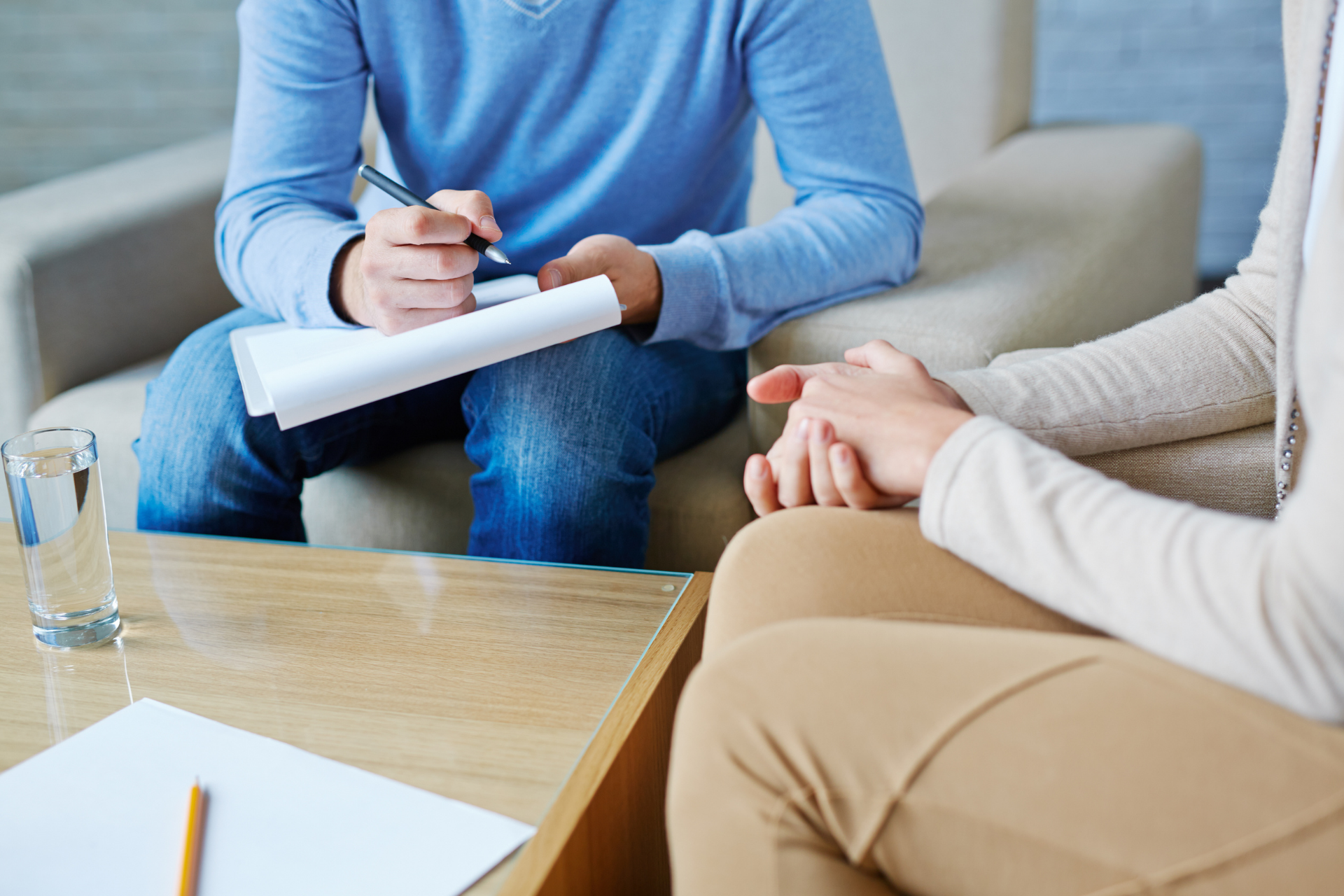 Therapist taking notes during a counseling session. A person sits with hands clasped.