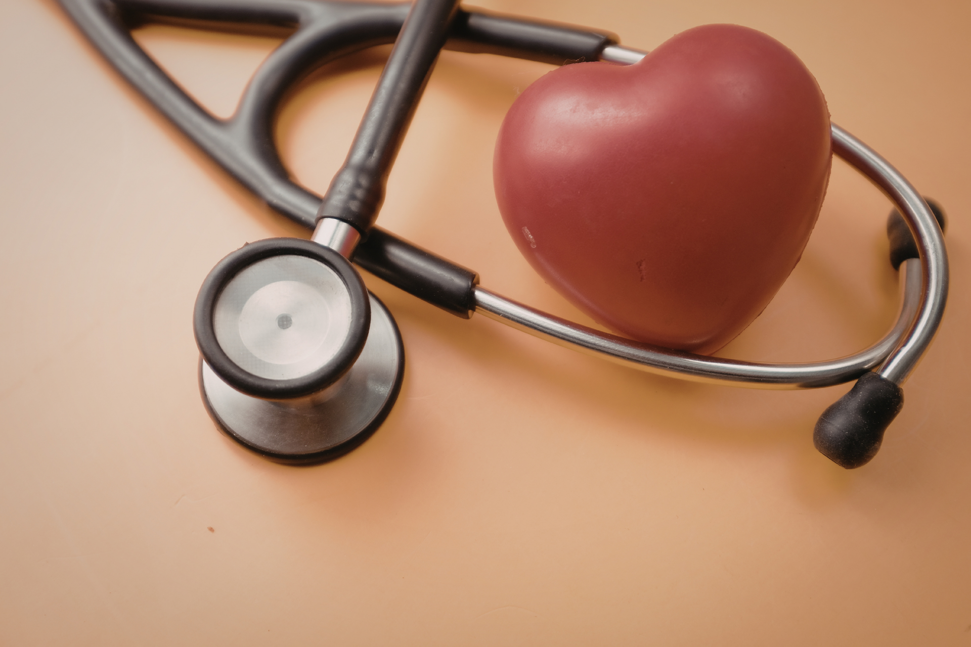 Stethoscope draped around a red heart, resting on a beige surface.
