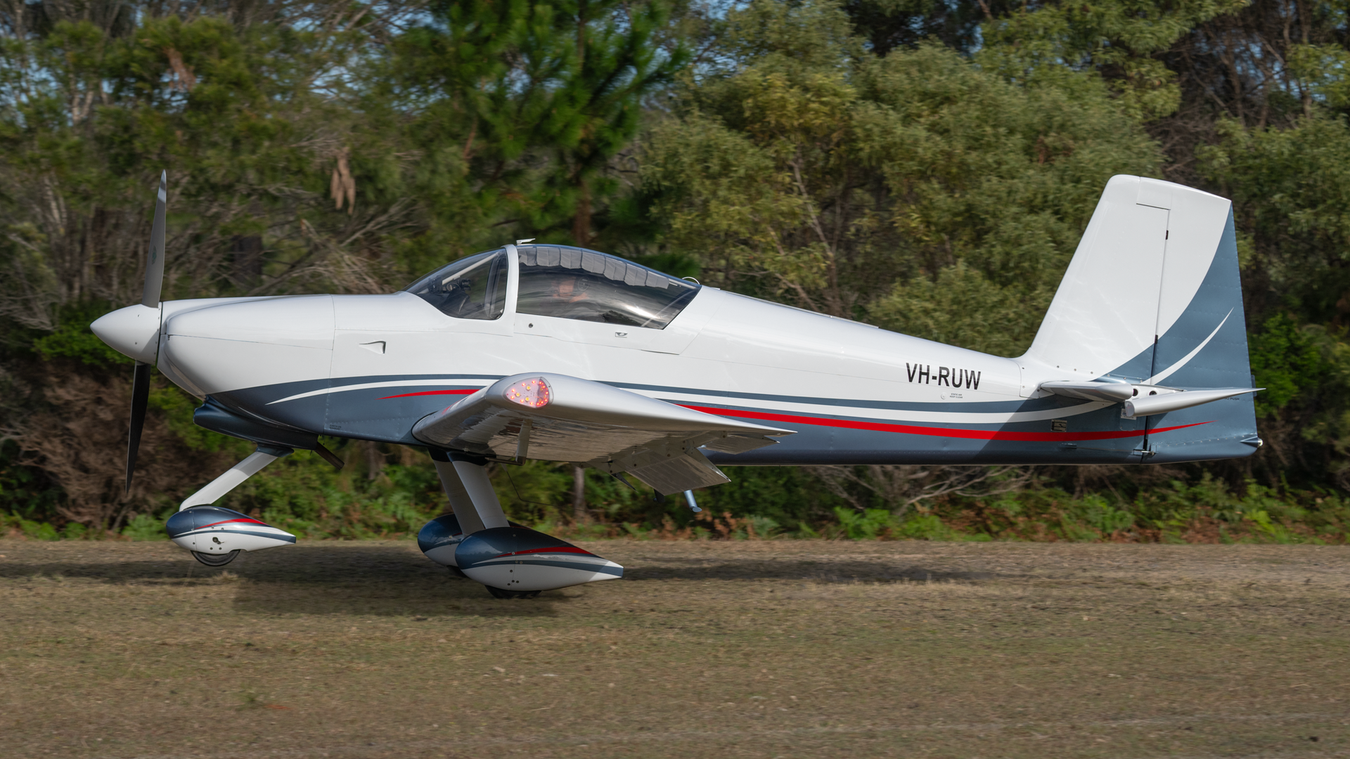 A small propeller plane is parked in a field with trees in the background