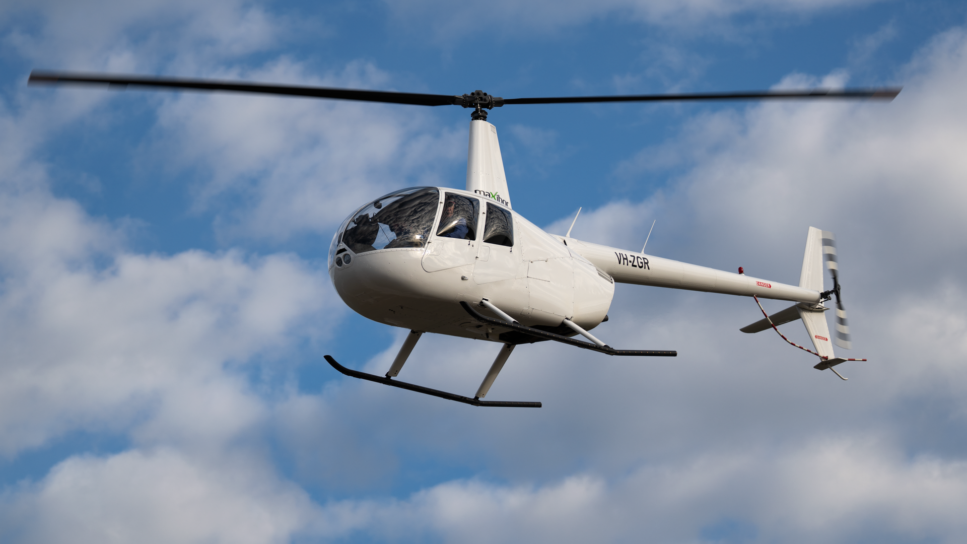 A small white helicopter is flying in the sky.