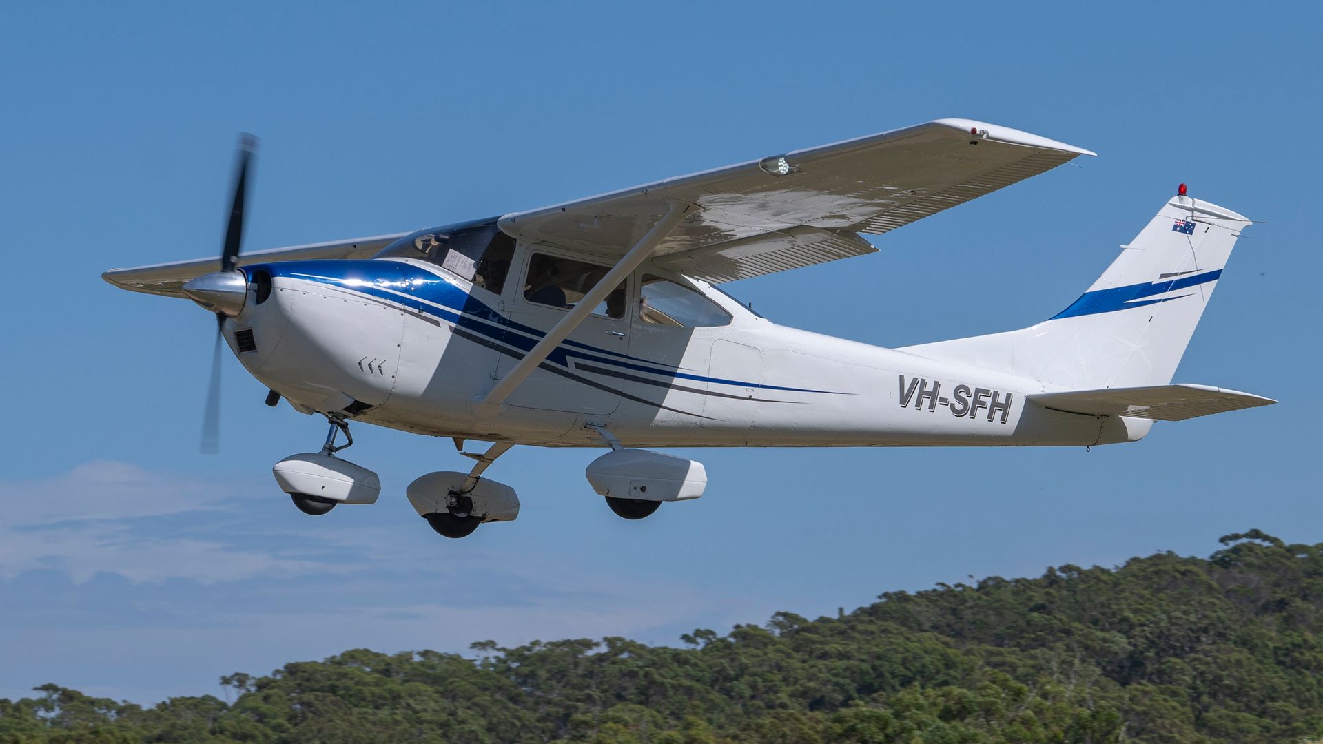 A small propeller plane is flying over a forest.