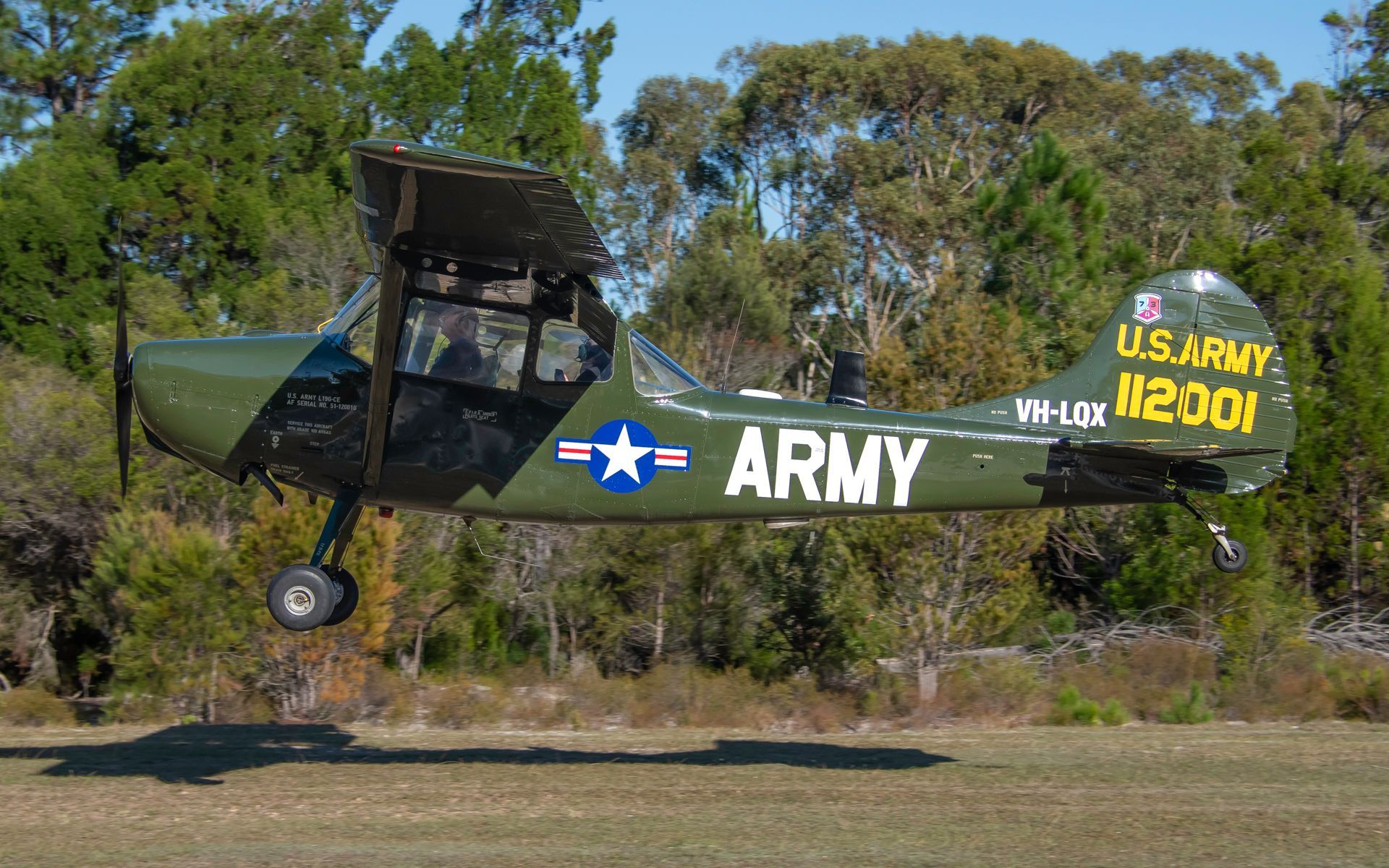 a green army plane is taking off from a grassy field