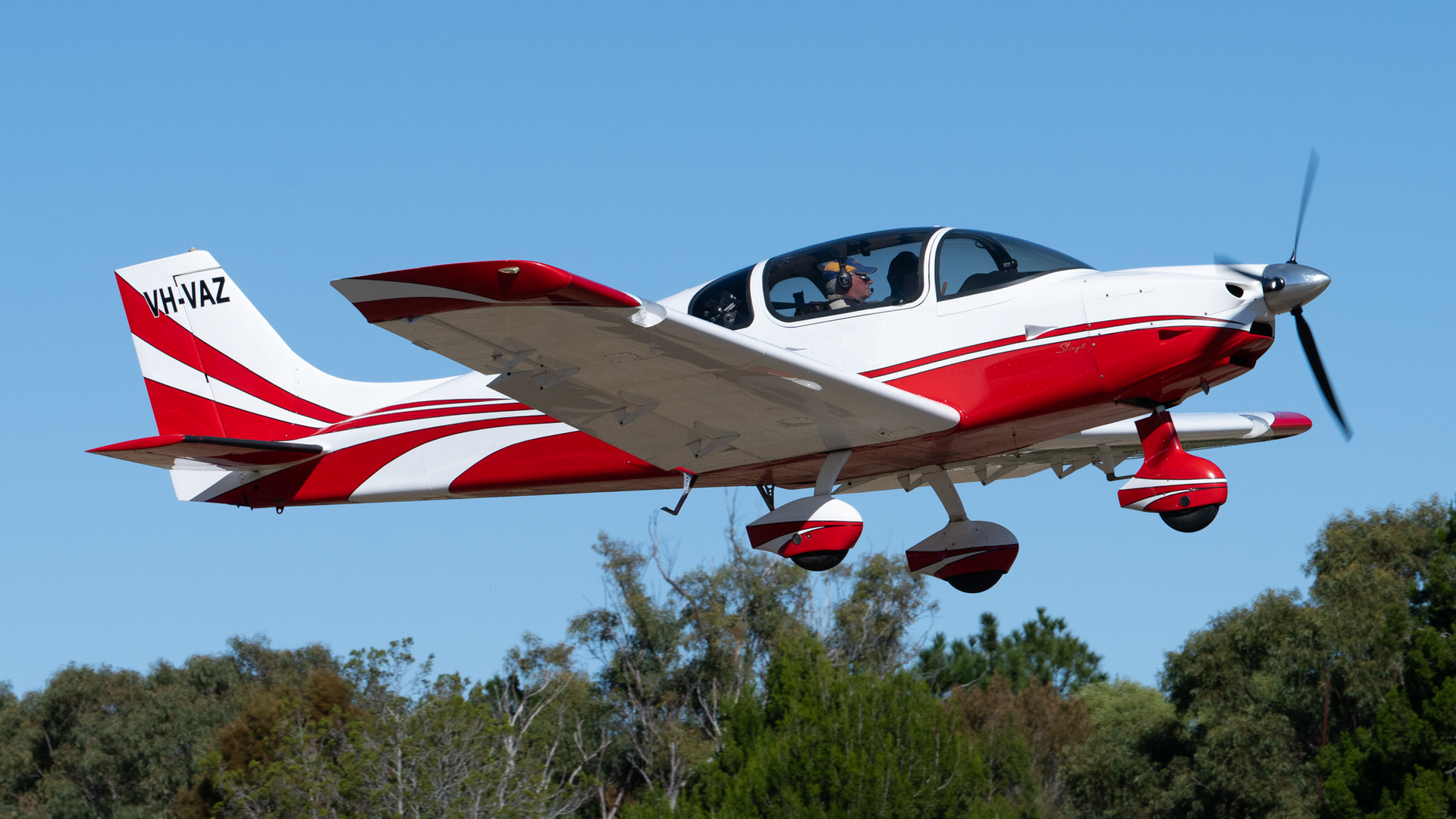 A small red and white plane with a propeller is flying in the sky