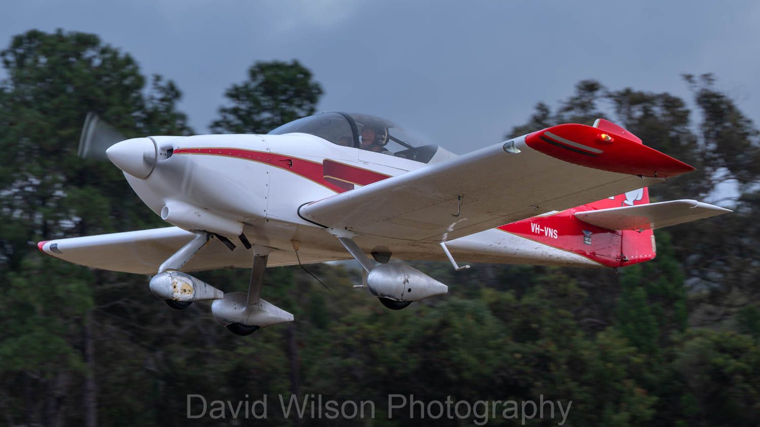 A small white and red airplane is flying in the sky by david wilson photography