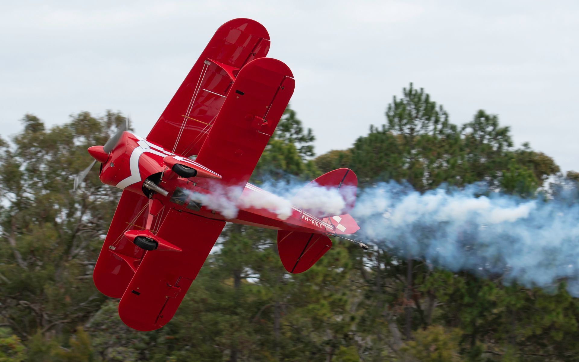 a red biplane is flying through the air with smoke coming out of its wings .