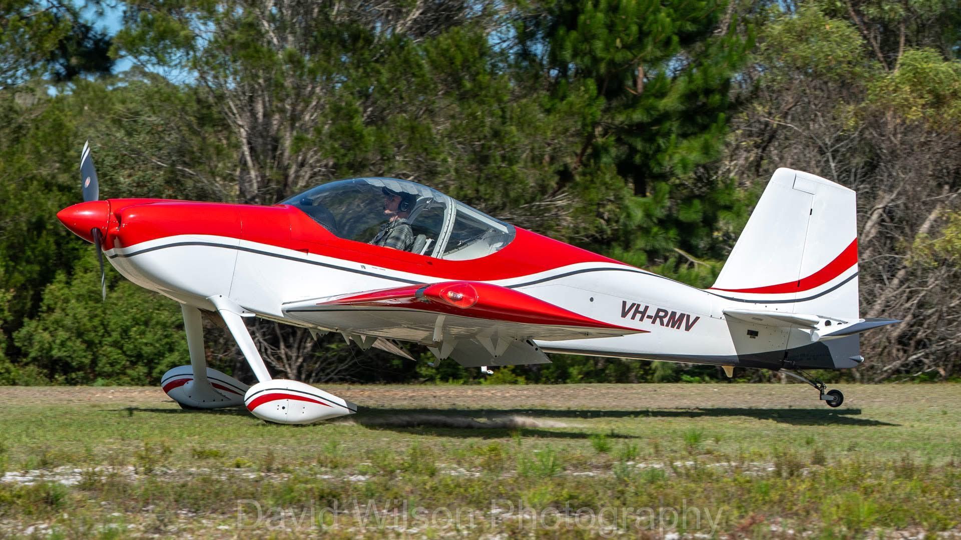 Red and white single-engine airplane parked on grass. VH-RWV tail number. Sunny day.
