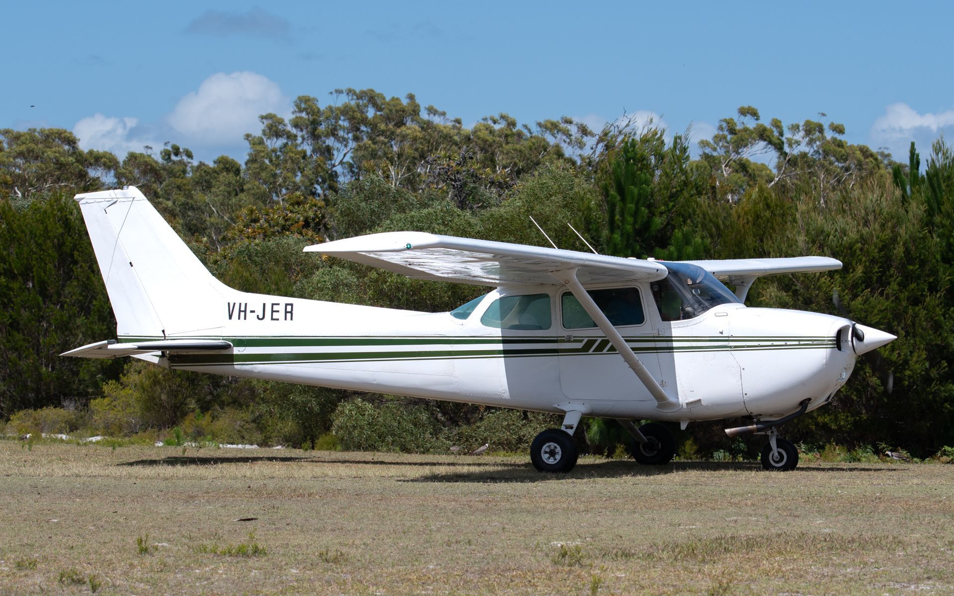 a small white plane with a green stripe on the side is parked in a field