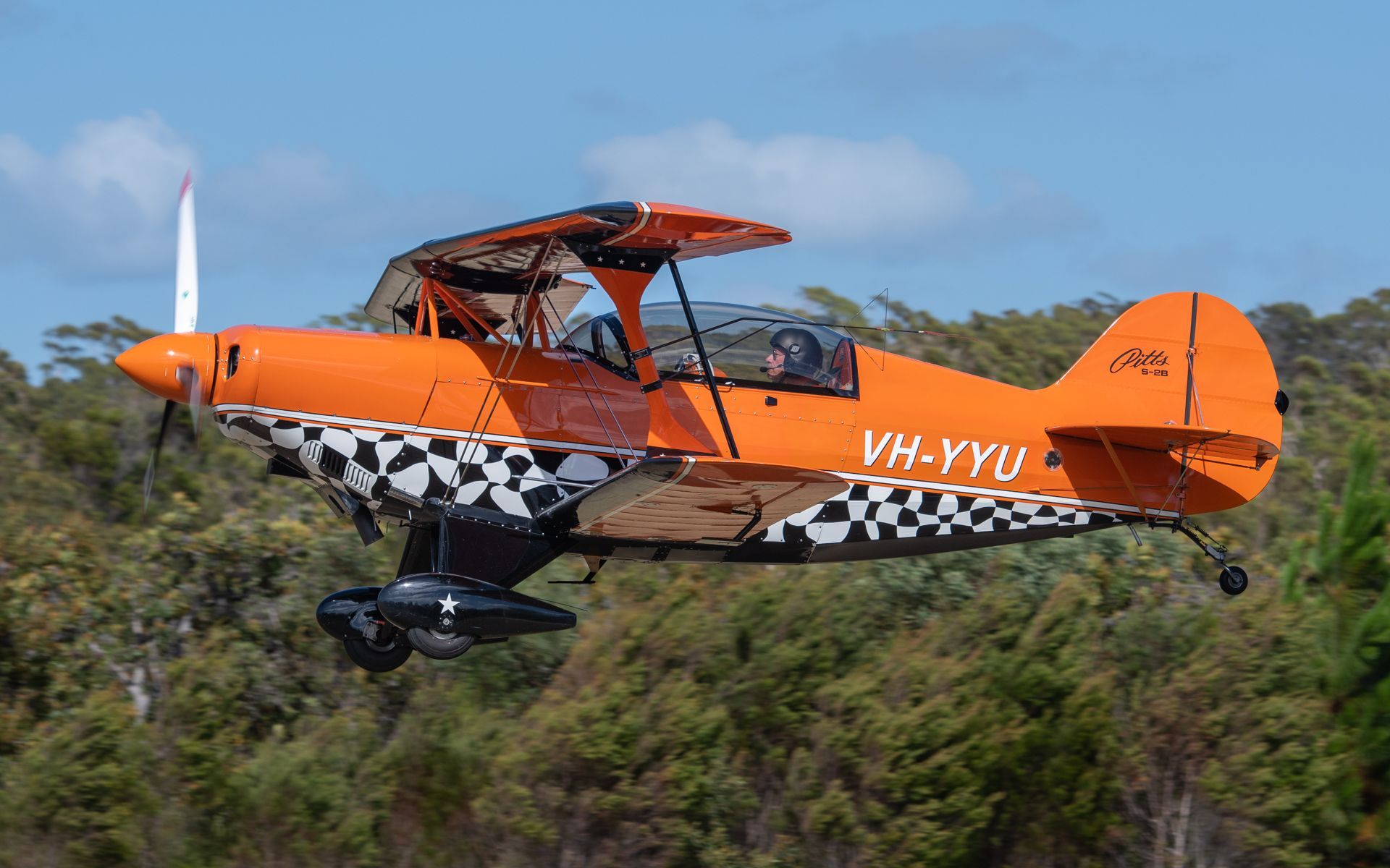 a small orange airplane is flying over a forest .