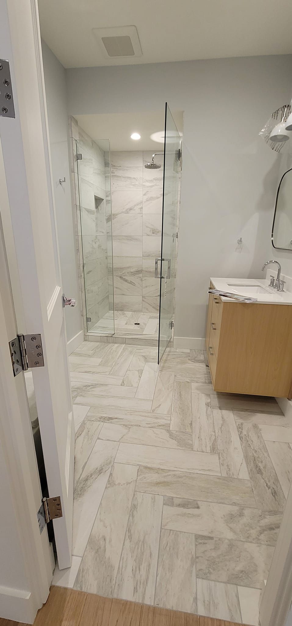 A bathroom with a walk in shower , sink and mirror.