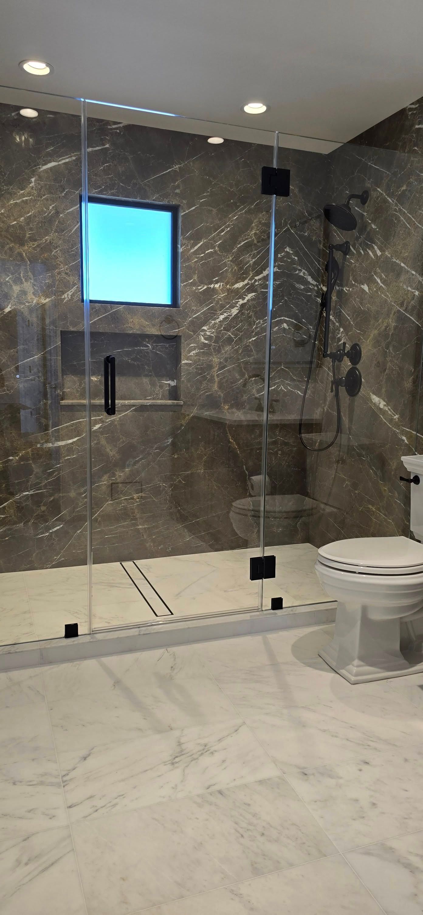 A bathroom with a walk in shower , toilet , sink and window.