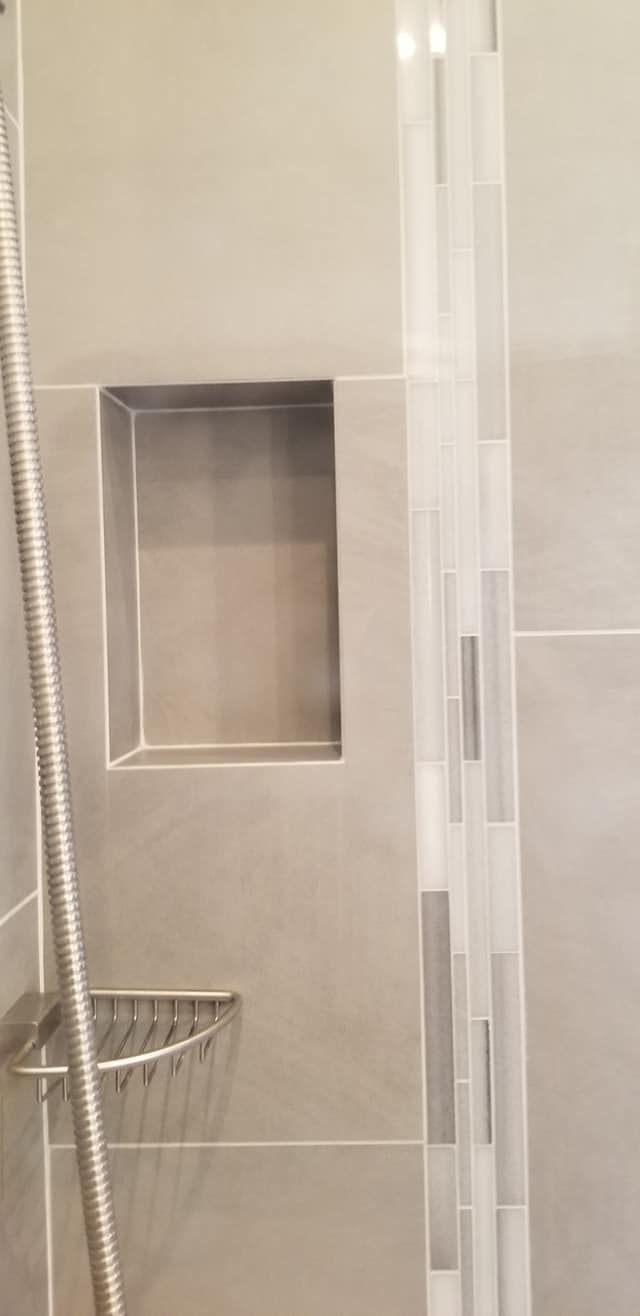 A close up of a shower with a shelf and a shower head.
