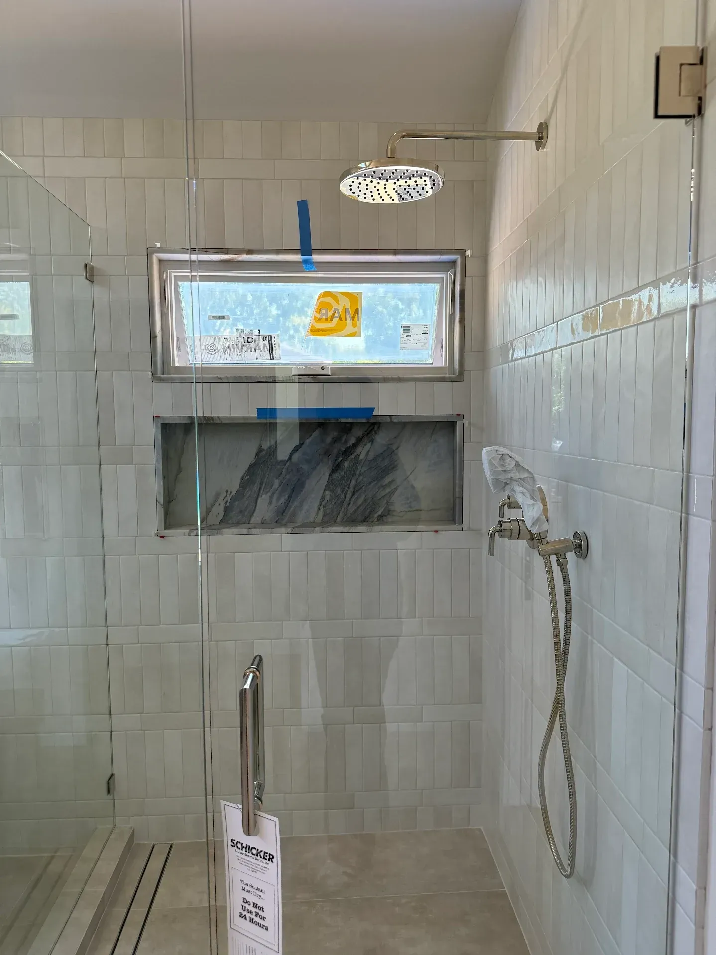 Shower with glass enclosure and tiled walls, featuring a window and recessed shelf with a dark marble accent.
