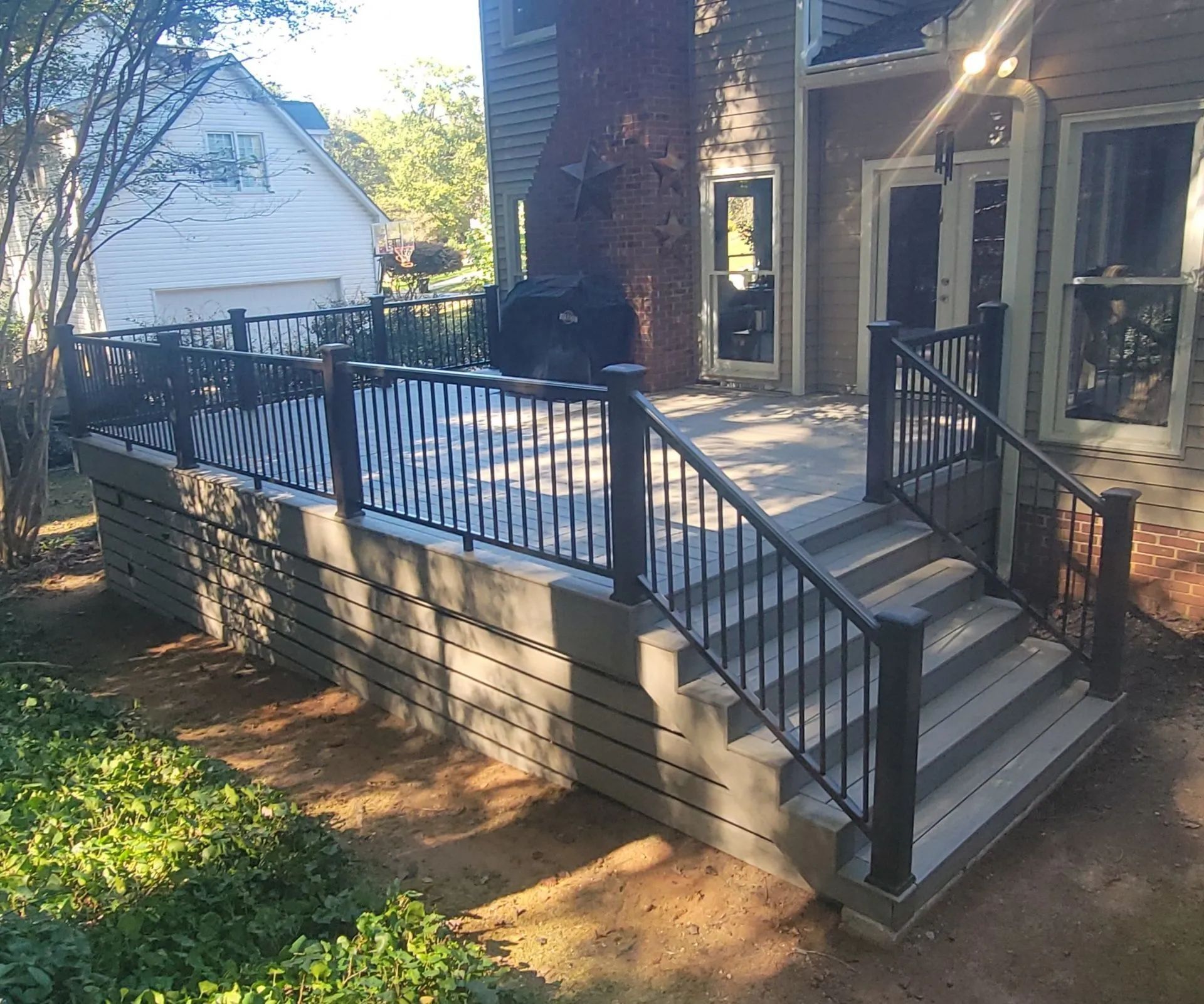 Composite deck with black railing and steps attached to a house with a surrounding yard.