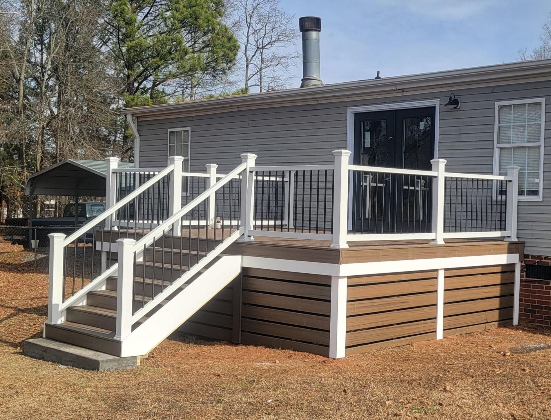 Wooden deck with white railings and black spindles, attached to a house with dark doors.