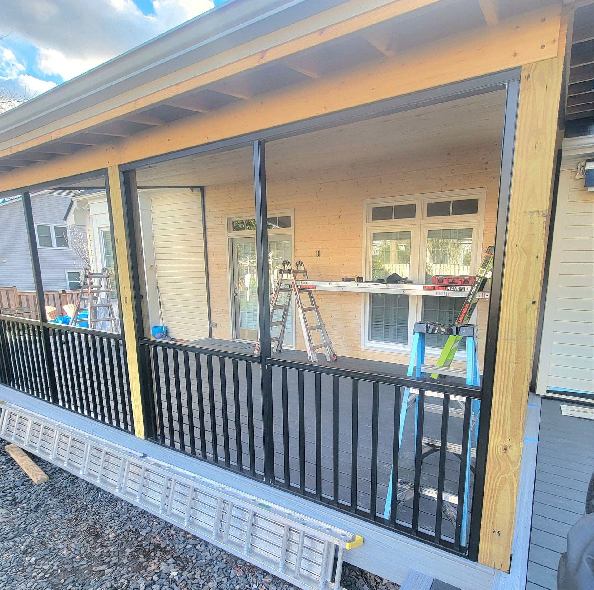 A porch under construction with a black railing, wooden posts, and a ladder leaning against the house.