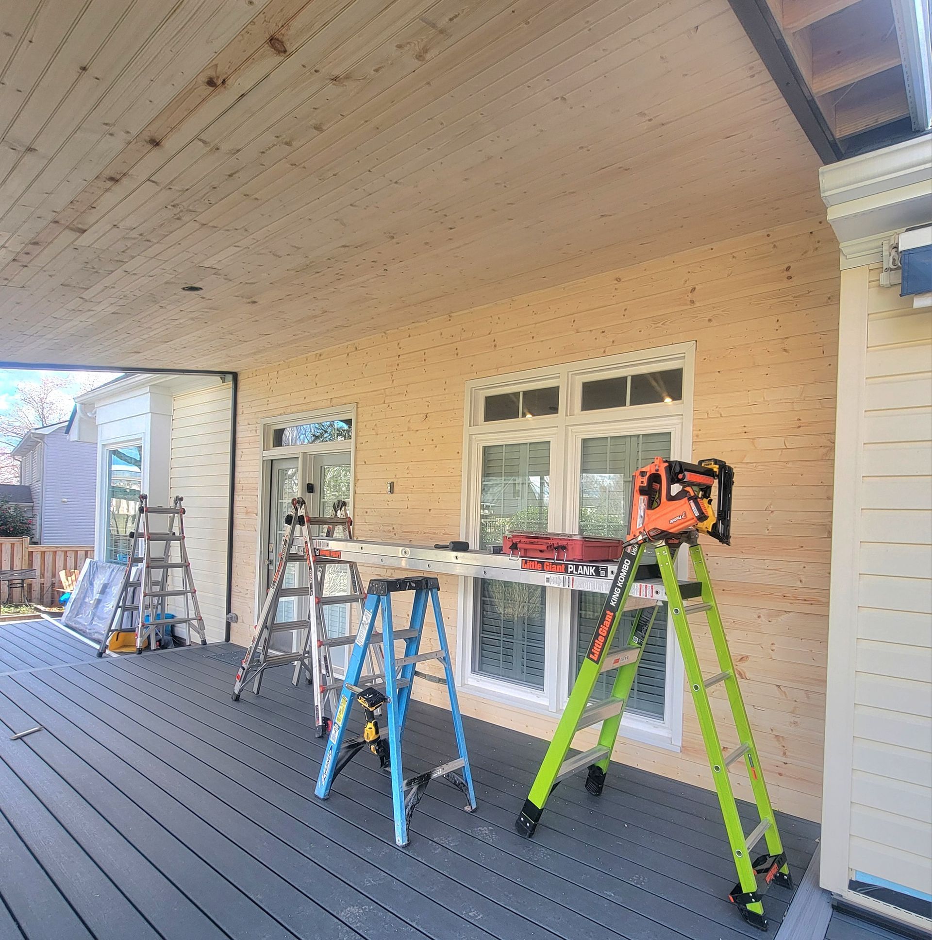 Construction site with ladders, tools, and materials on a covered deck with new siding.