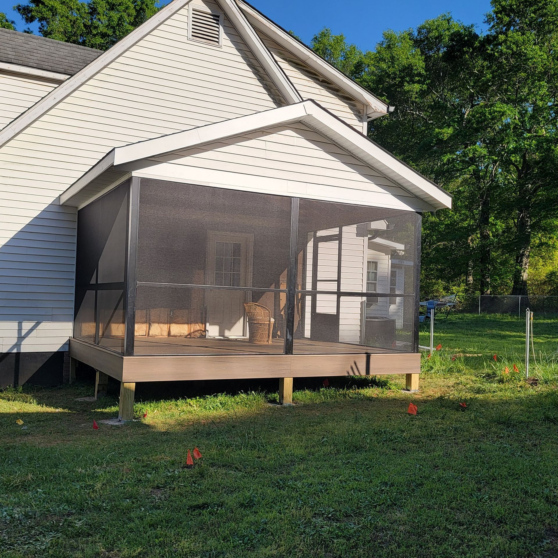 Screened porch attached to a white house, on a wooden deck, surrounded by green grass.