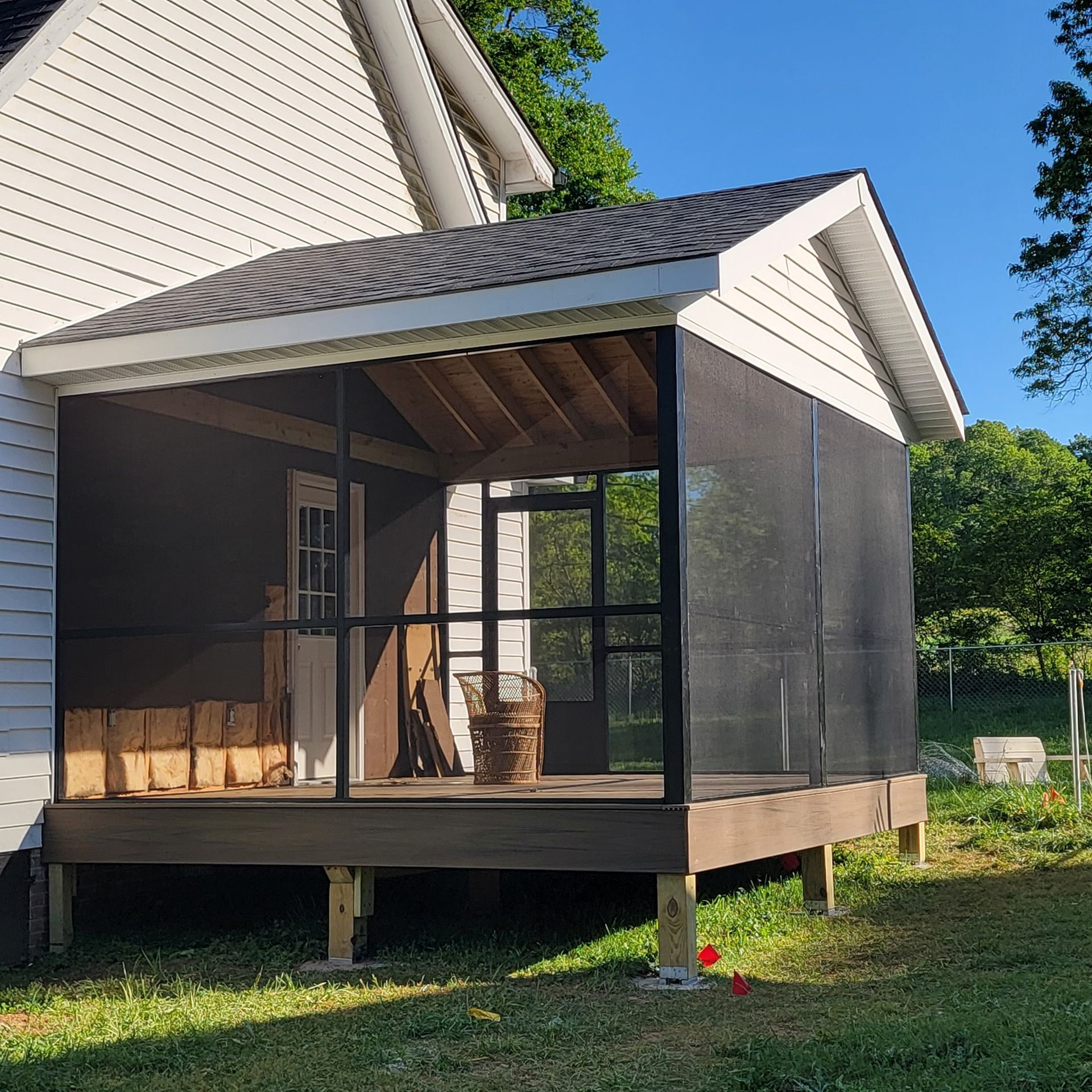 Screened-in porch attached to a white house with a dark roof and wooden deck.