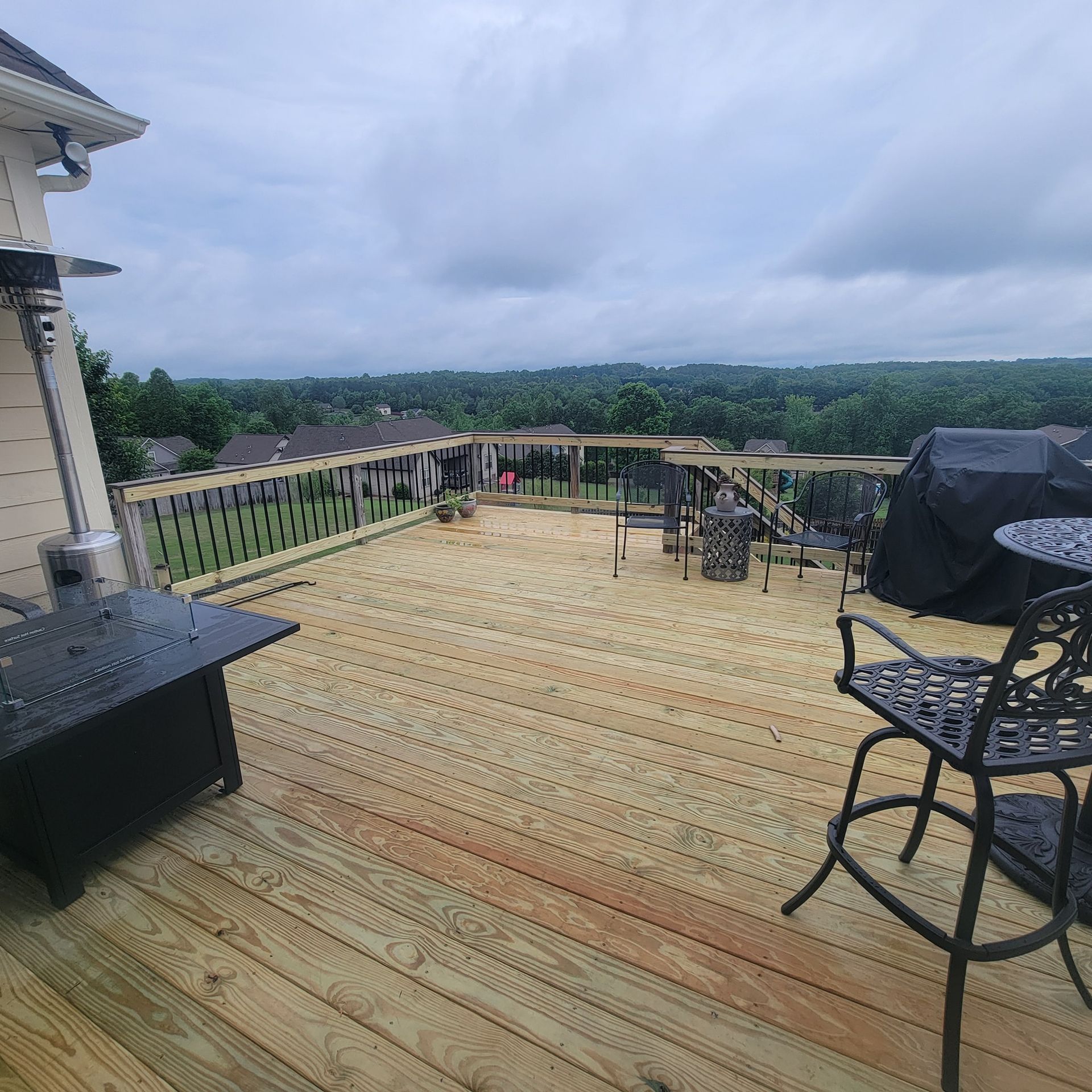 Large wooden deck with outdoor furniture overlooking a treeline, under a cloudy sky.