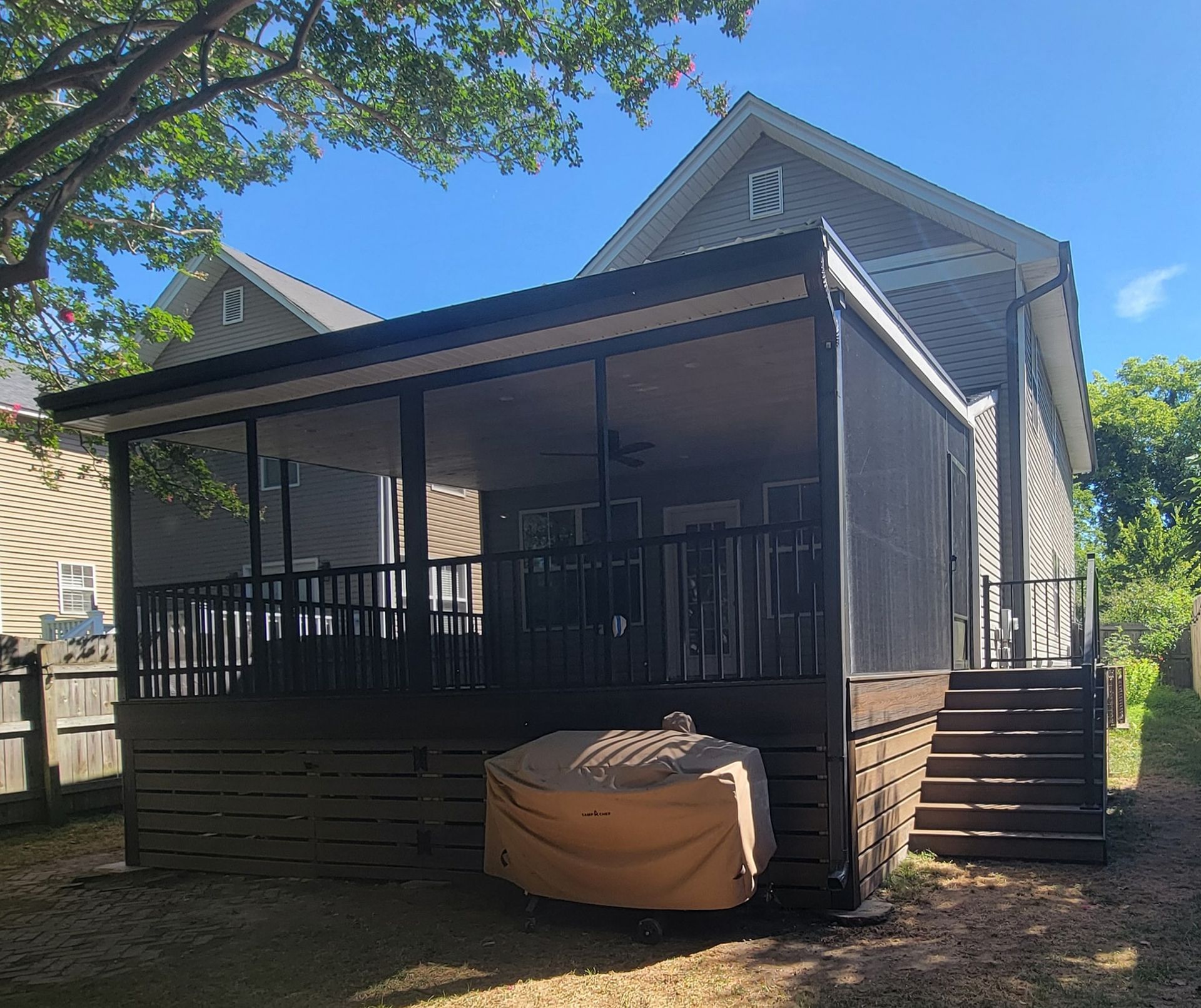 Screened porch attached to a house; brown deck, black railings, tan screen, brown cover on a small tub.